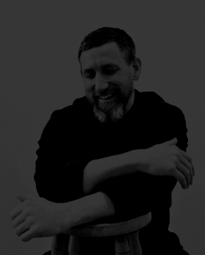 Matt is smiling whilst leaning his loosely crossed arms on a stall. His greying beard is quite something.