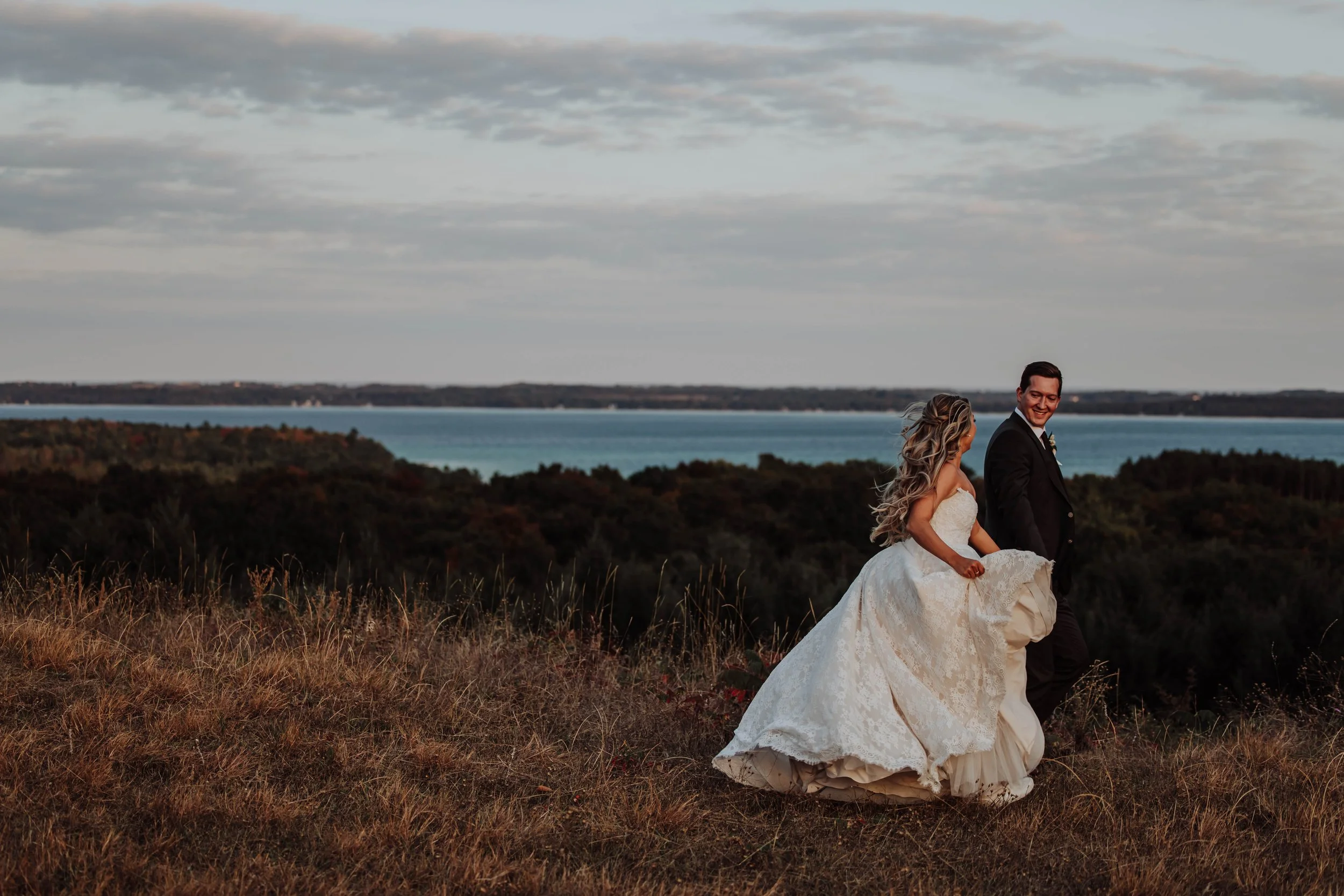 Couple embracing on a grassy bluff overlooking the lake at dusk at Black Star Farms wedding venue Traverse City, Michigan