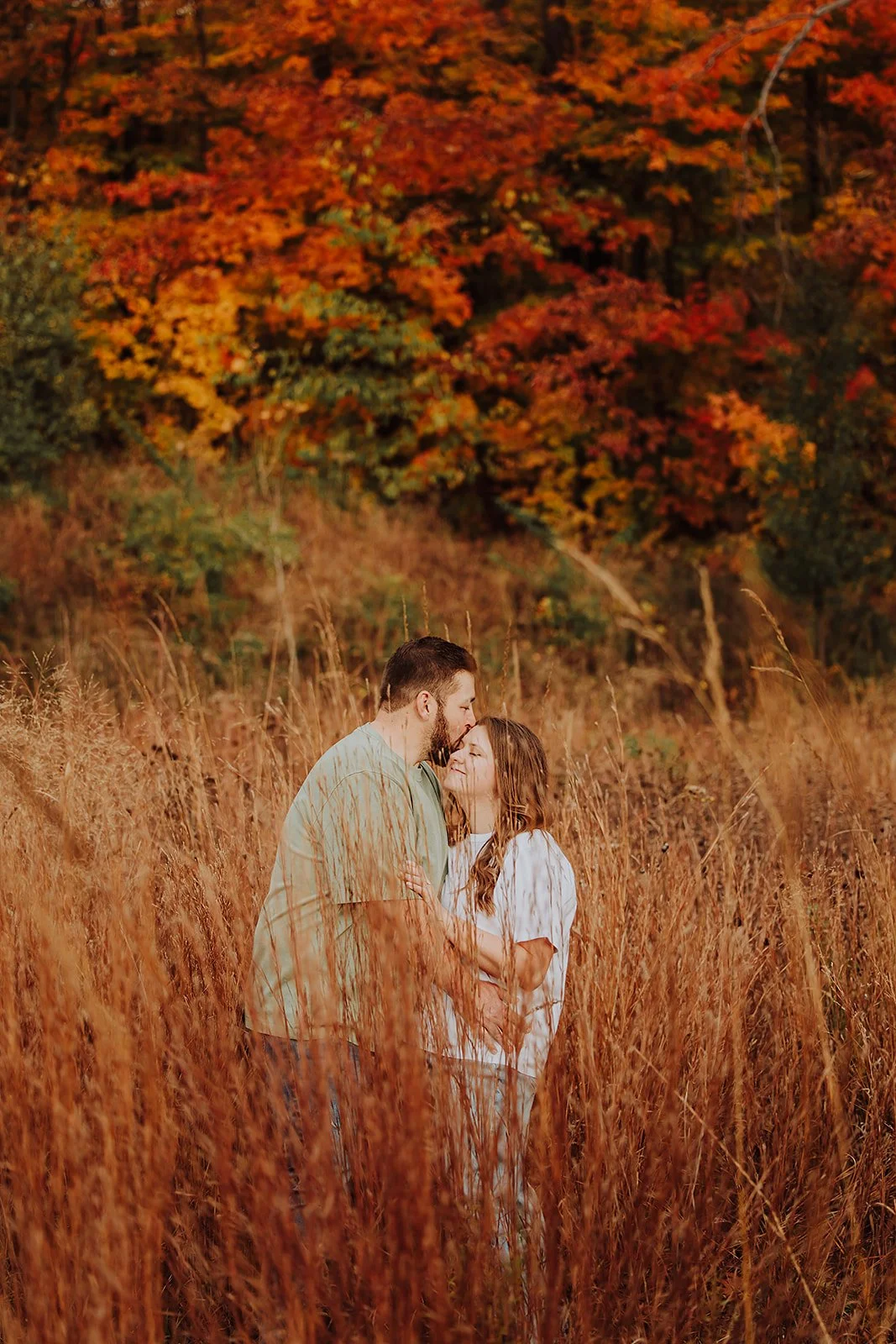 Forehead kiss in tall golden grass during a fall engagement session in West Michigan