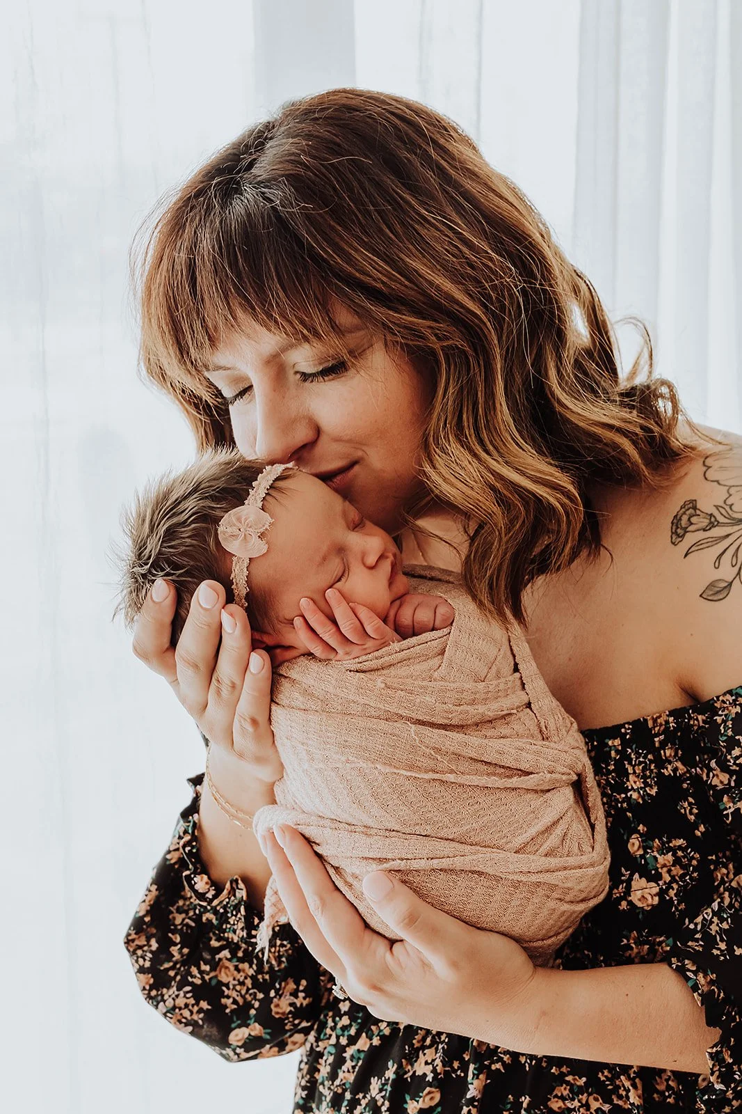 Lexie kissing her newborn baby in soft window light