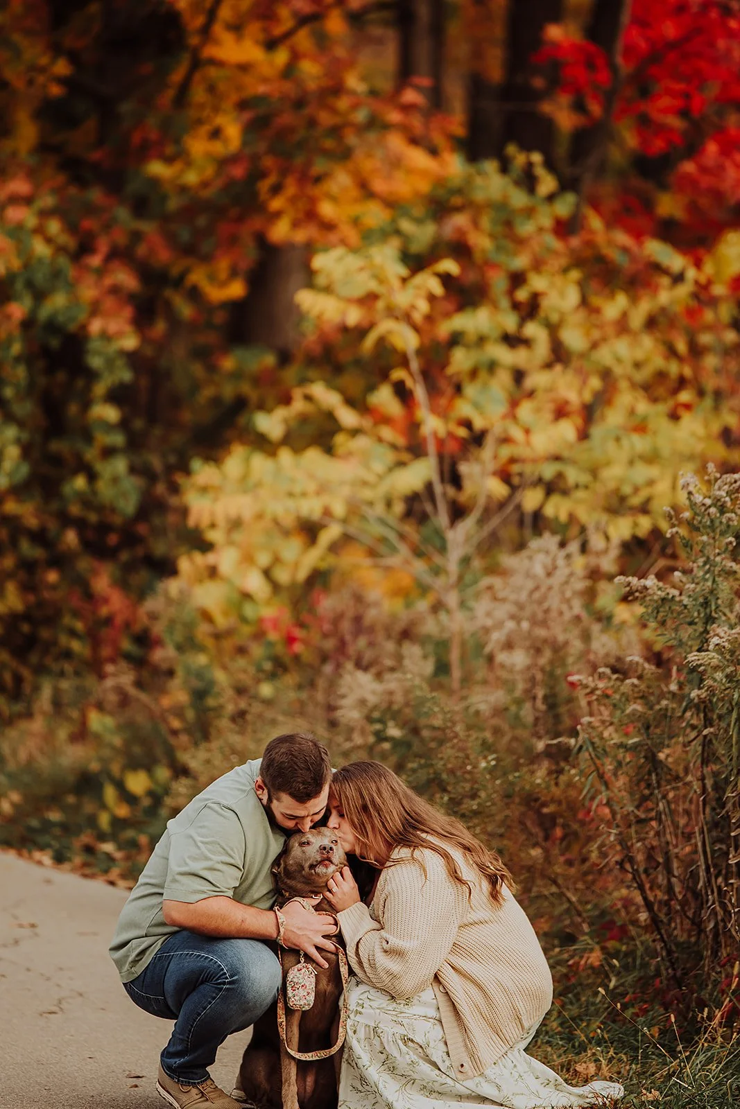 Couple kissing their dog on a fall trail, West Michigan engagement photos