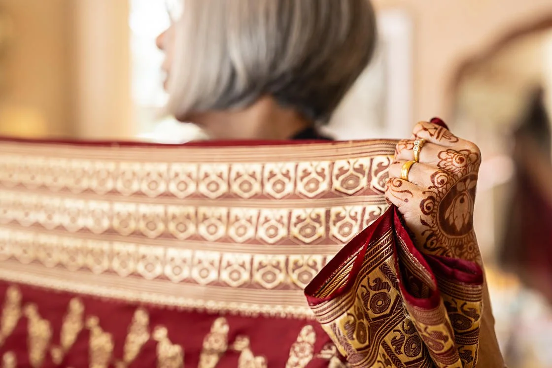 Close-up of a woman holding a richly decorated red and gold shawl with henna designs on her hand.