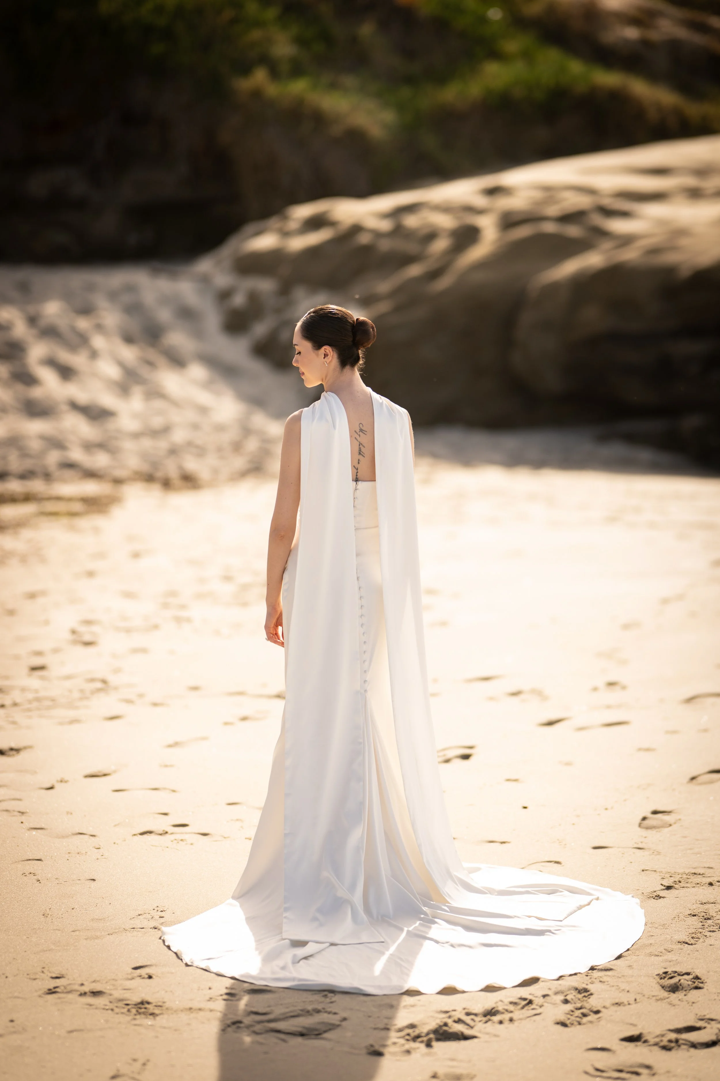 A woman in a white dress standing on sandy beach with rocky cliffs in the background.