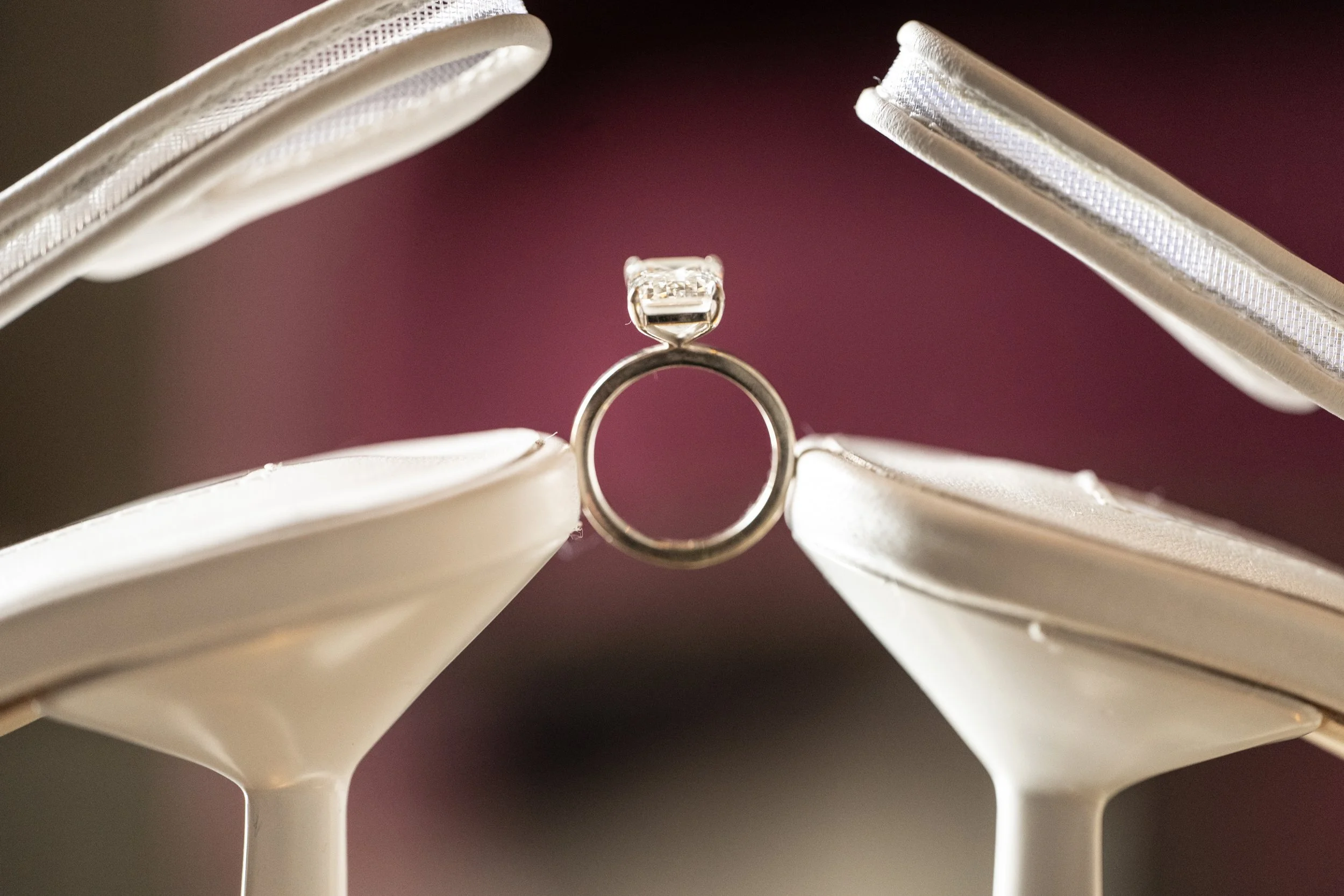 A close-up of a diamond engagement ring displayed between two white open jewelry boxes, with a dark background.