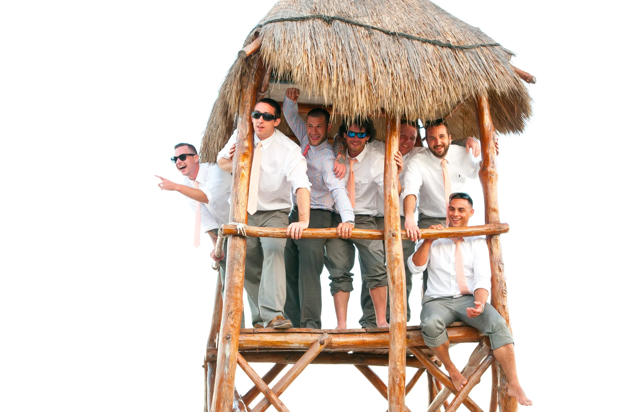 Group of men in shirts and ties enjoying themselves on a wooden structure with a thatched roof, possibly a tiki hut, against a plain white background.