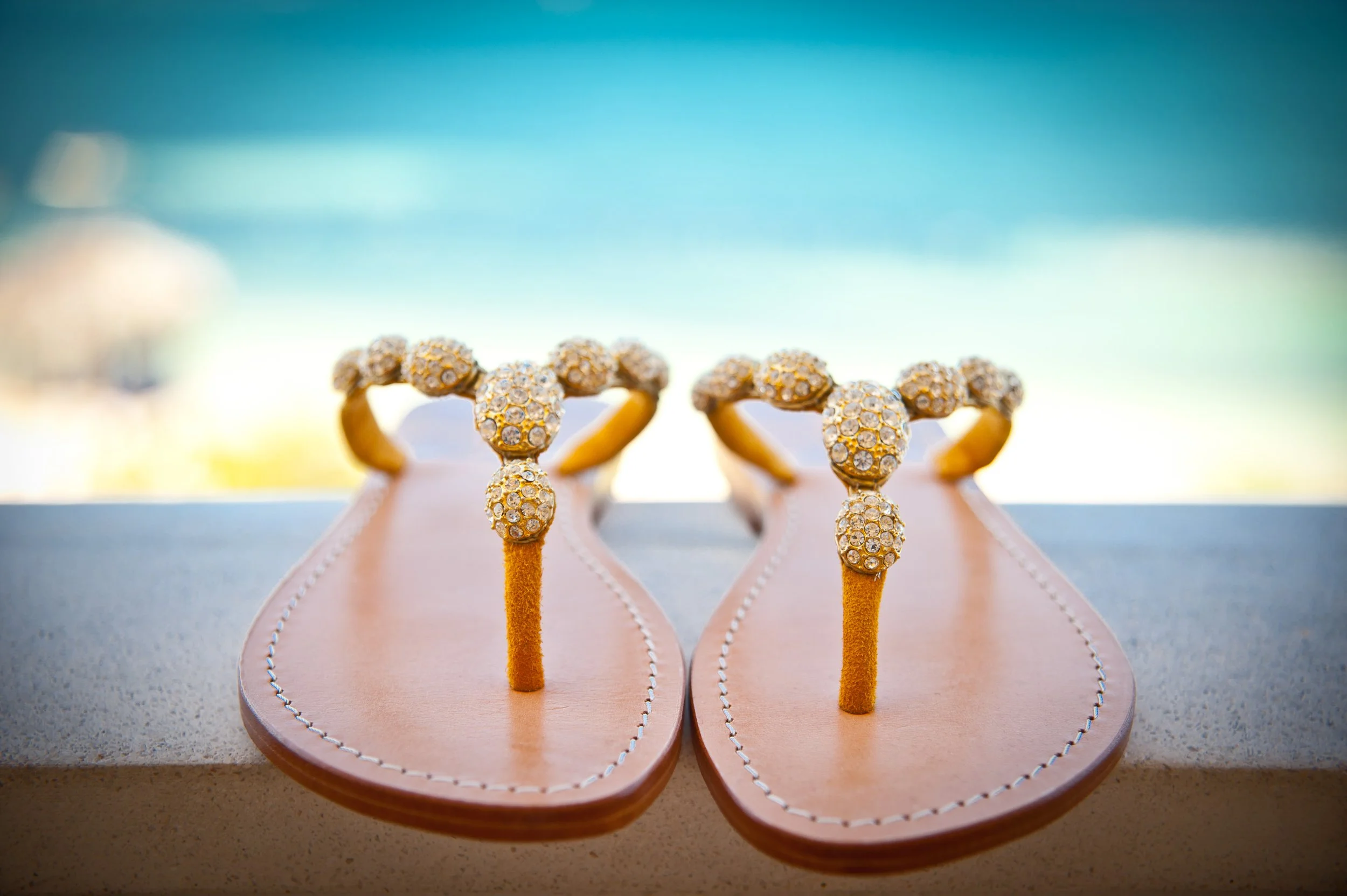 Pair of pink sandals with glittering gold and diamond-adorned straps, placed on a countertop with a blurred background.