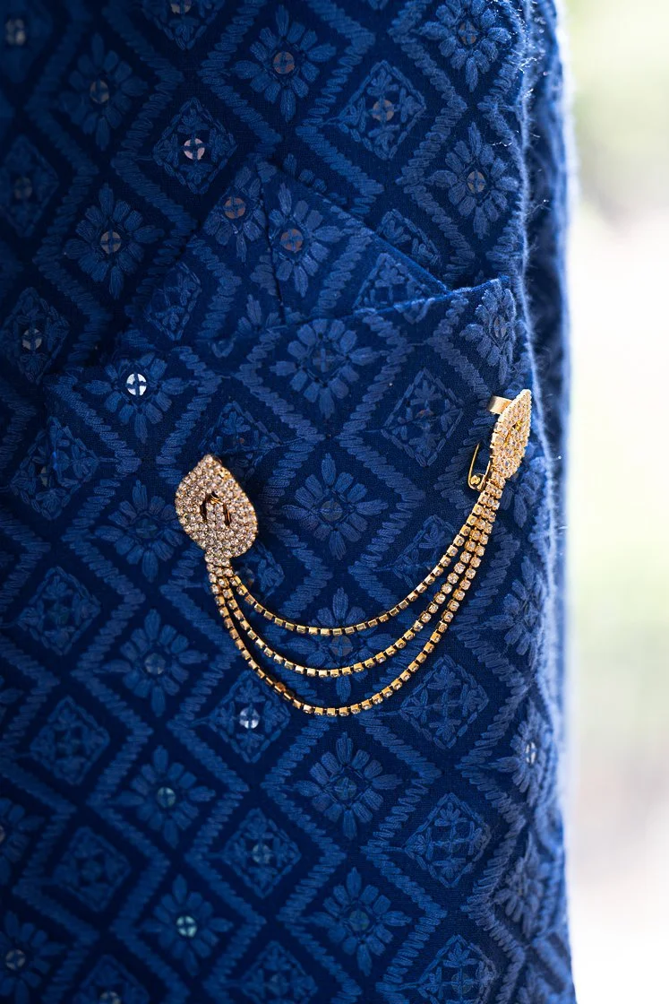Close-up of a blue embroidered fabric with gold and rhinestone jewelry attached.