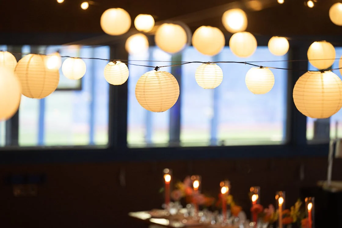 String of hanging paper lanterns with warm glow indoors, blurred background with windows.