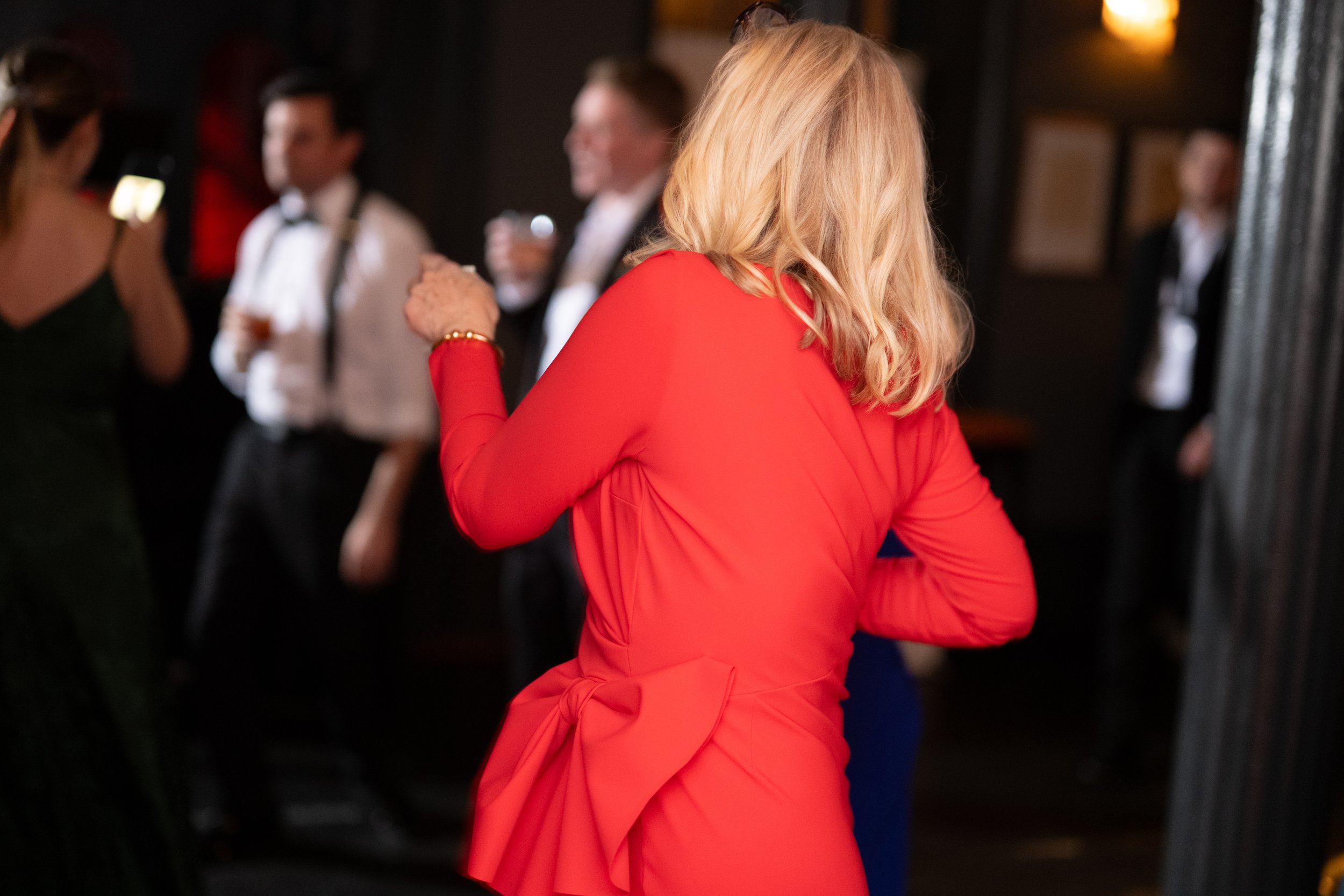 A woman with blonde hair in a red dress at a social event, with other people in the background.