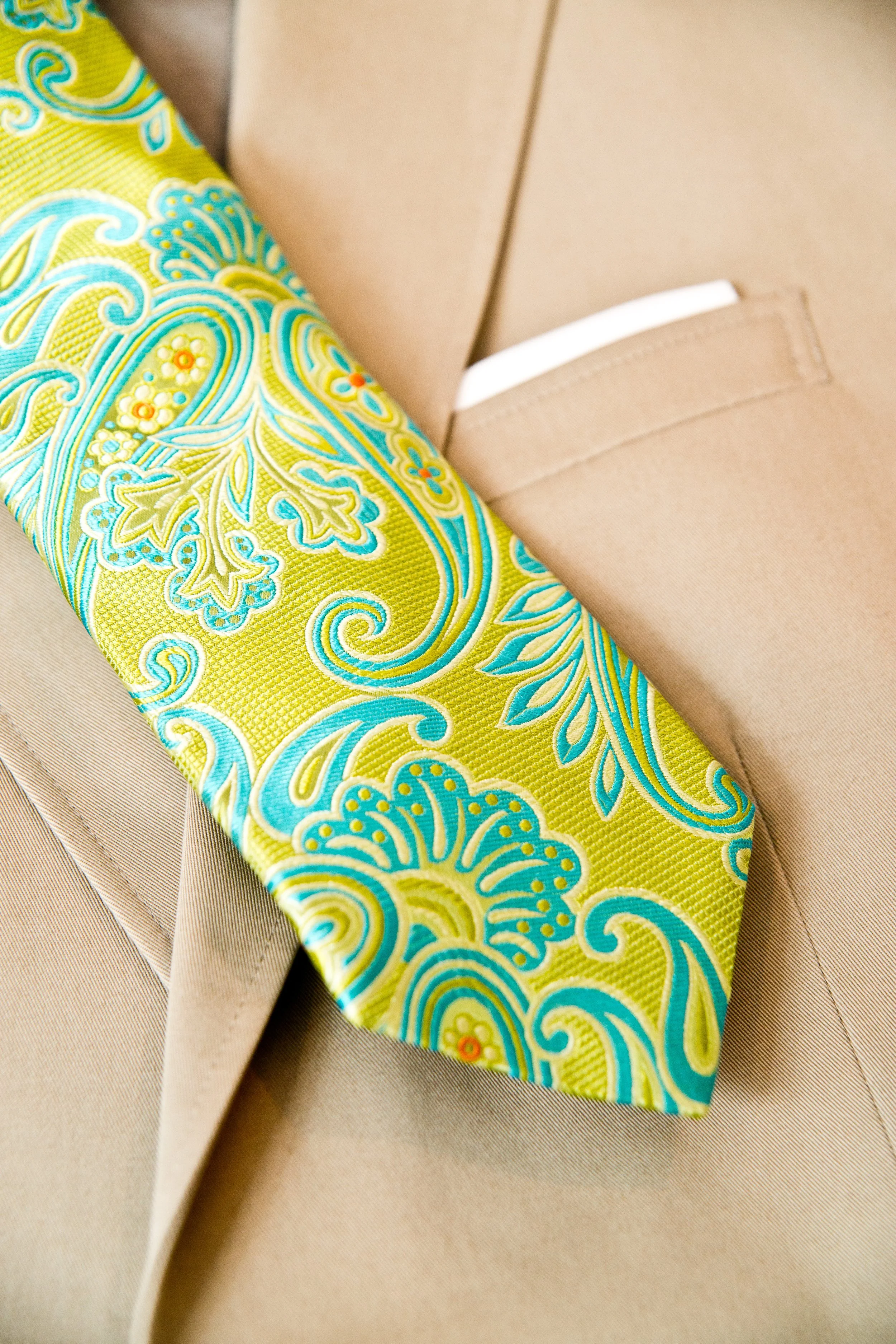 Close-up of a beige fabric suit with a colorful paisley tie in yellow, turquoise, and orange hues.