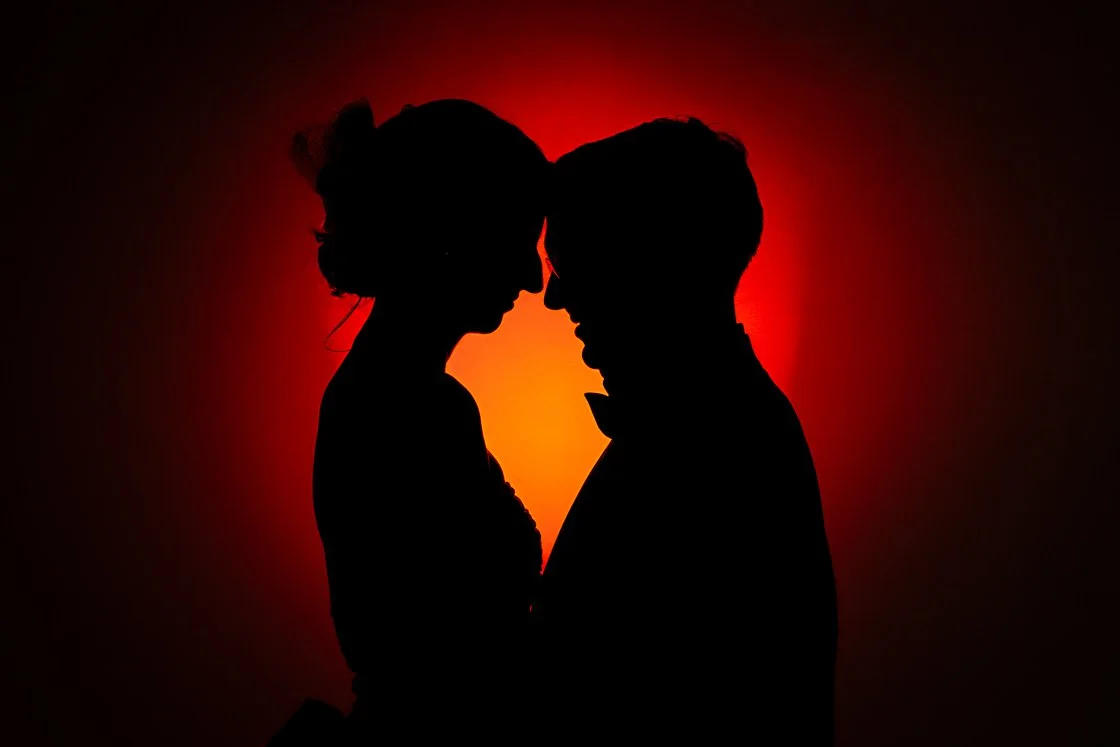 Silhouette of a couple facing each other with foreheads touching, set against a red and orange glowing background.