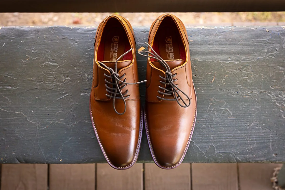 Pair of brown leather dress shoes with laces, placed on a weathered dark gray wooden surface.