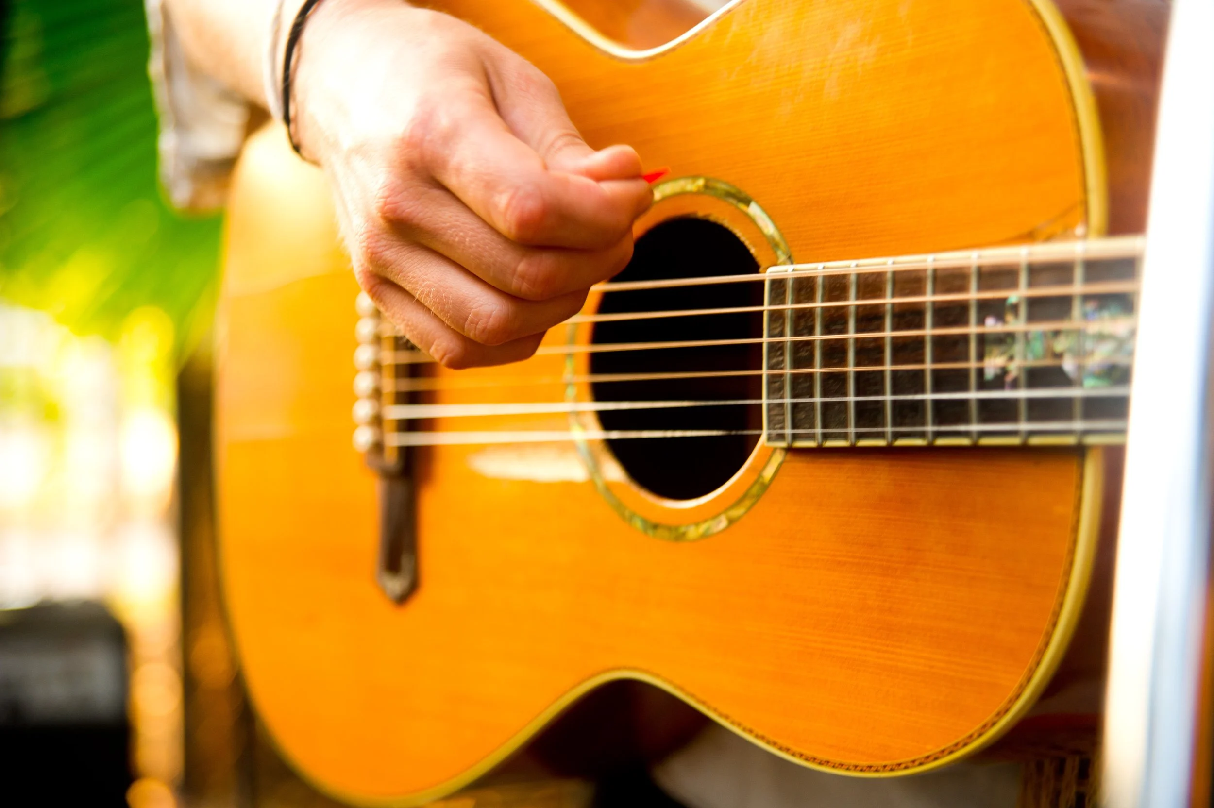 Close-up of a person playing an acoustic guitar outdoors, fingers pressing down on the strings near the sound hole.