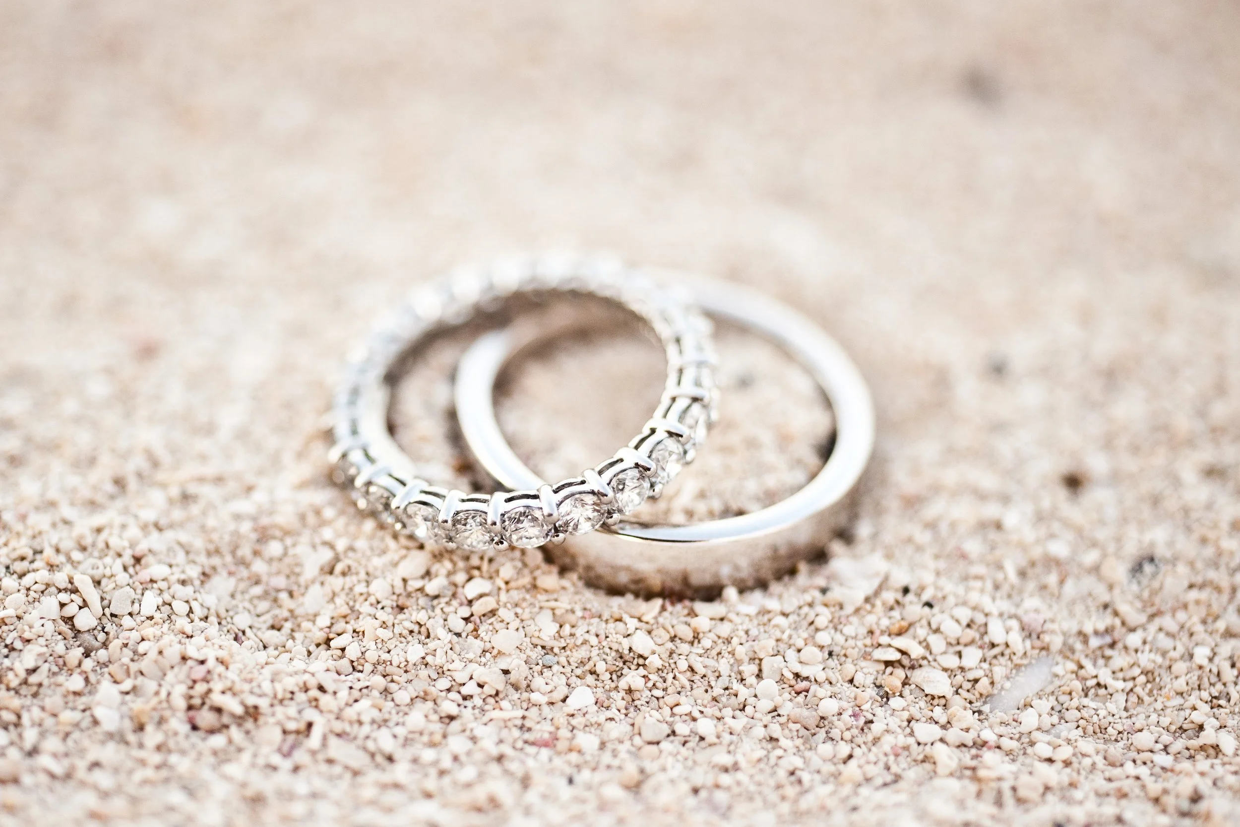 Close-up of diamond engagement rings on a sandy surface.