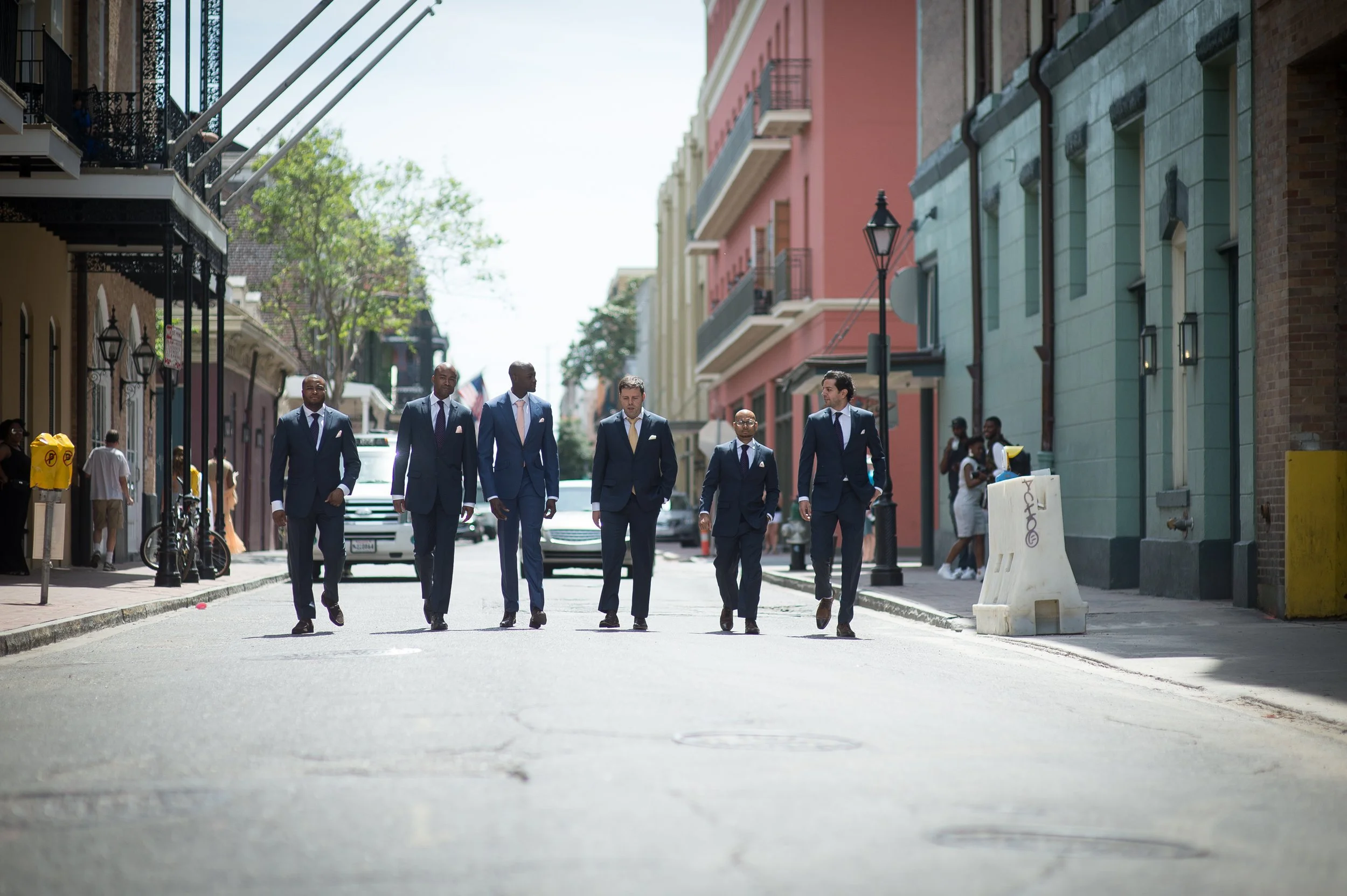 A group of men in suits walking down a city street on a sunny day.