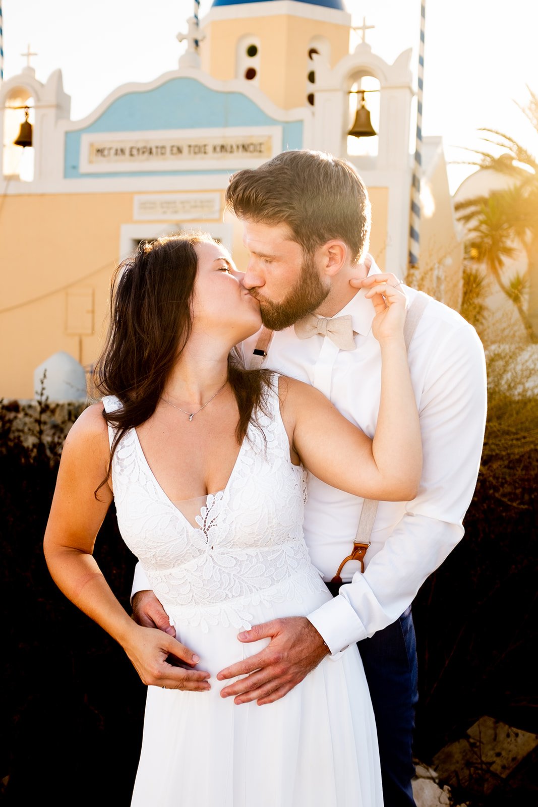 A couple sharing a kiss during a wedding or romantic event outdoors with a church in the background.