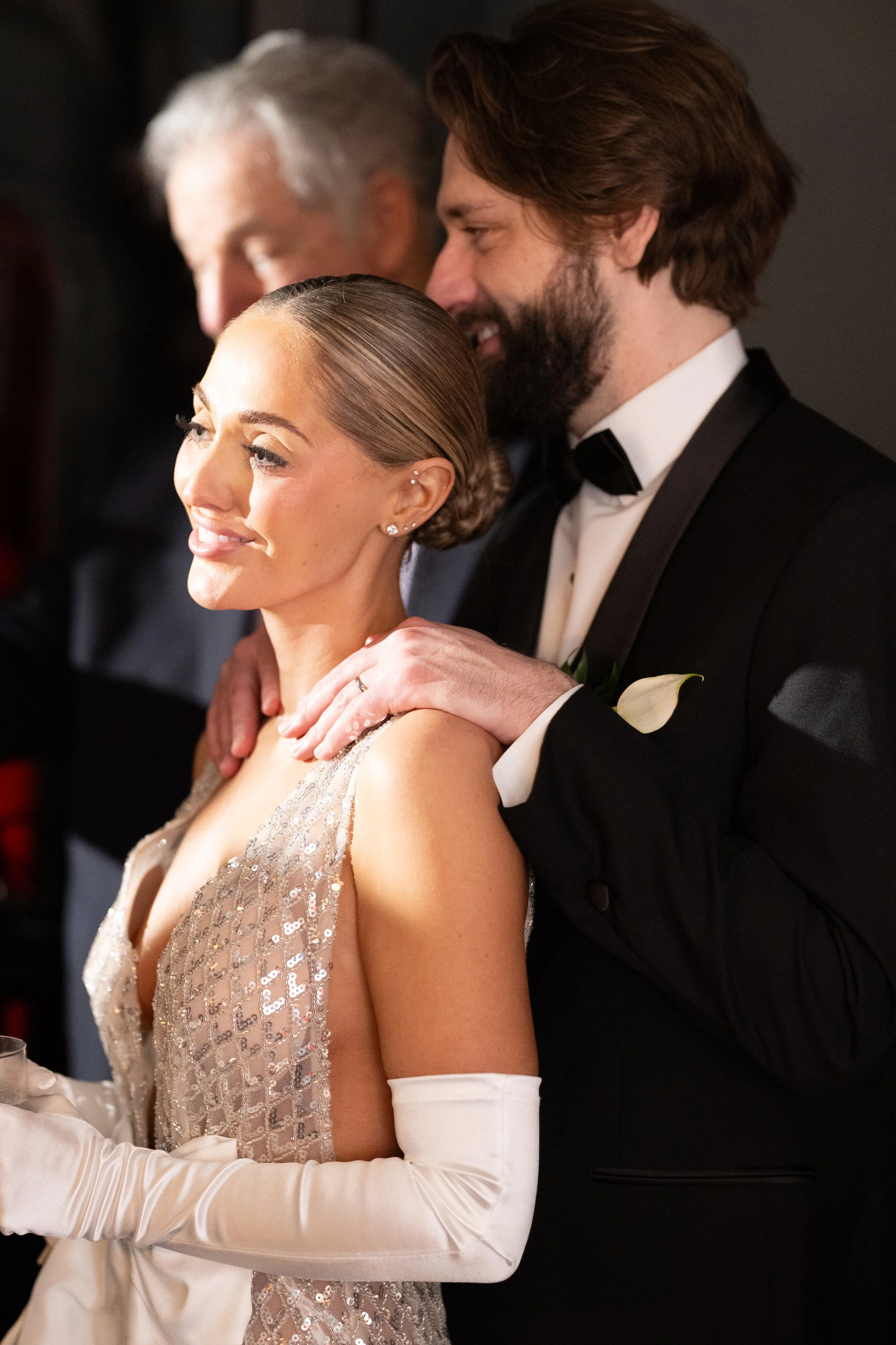 A bride and groom share a tender moment during their wedding, with the groom holding the bride from behind and both smiling.