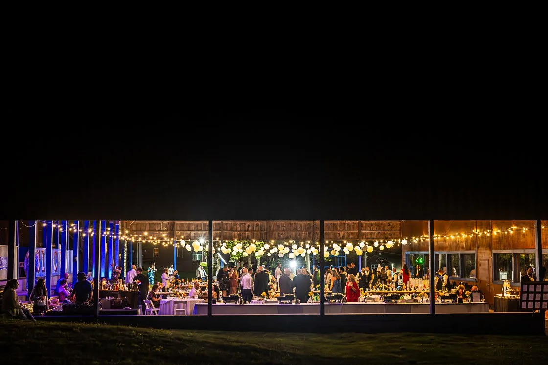 Indoor celebration with string lights and floating lanterns, people socializing and dining at tables.