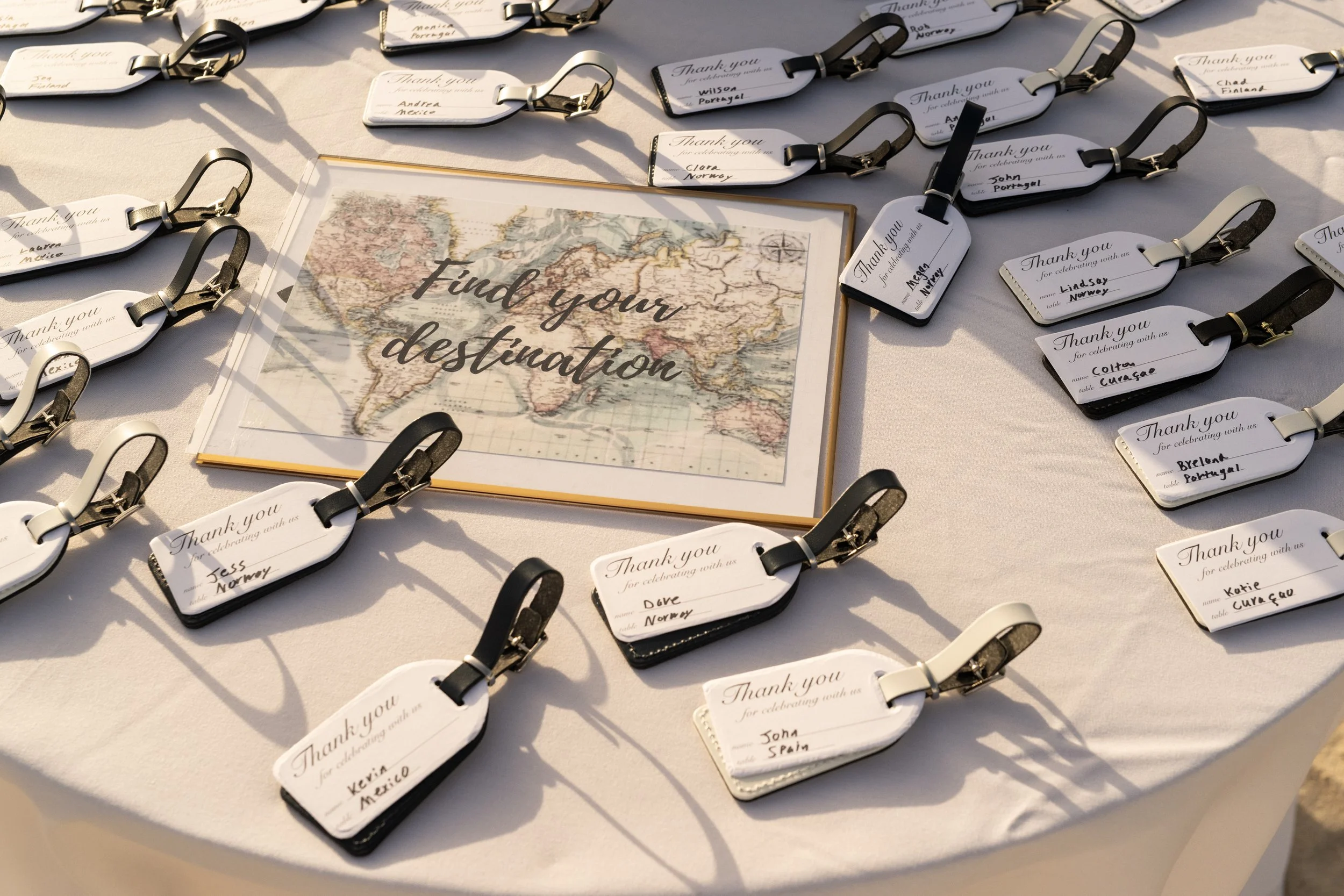 Multiple luggage tags with black and white straps on a table, with a framed map that says 'Find your destination' in the center.