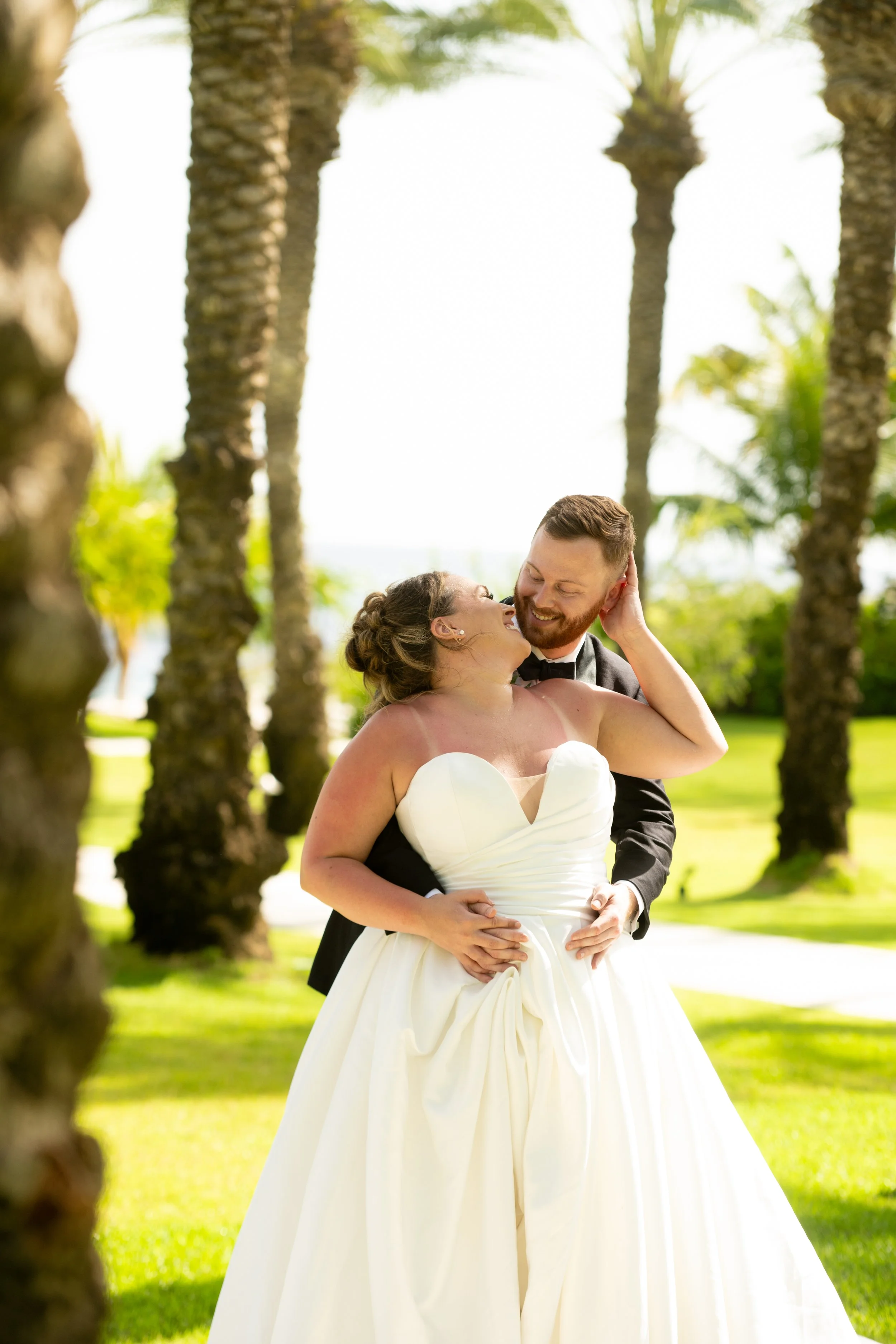 A newlywed couple embracing outdoors among palm trees on a sunny day.