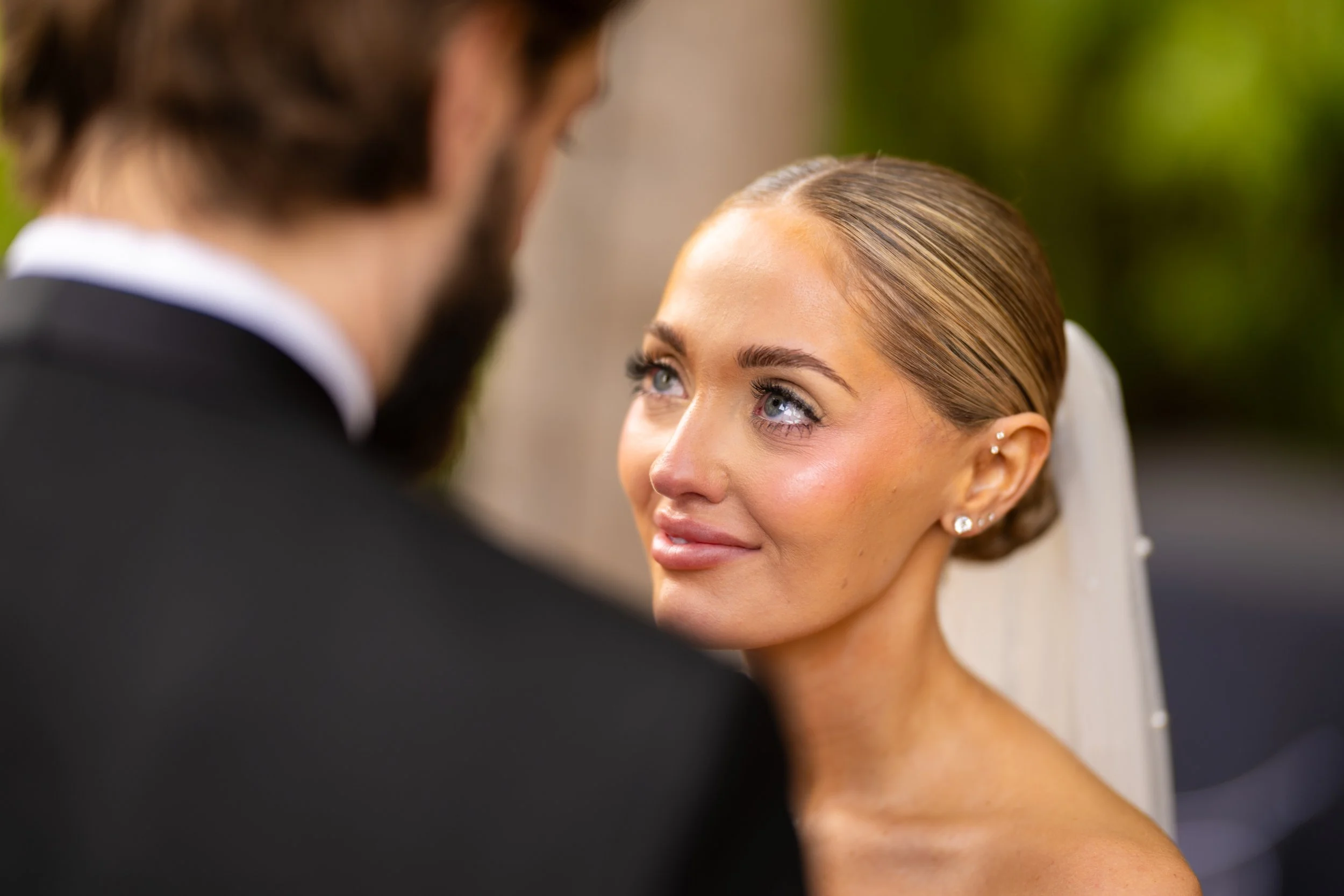 Close-up of a bride looking at her groom during a wedding ceremony, with focus on her face and eyes, and blurred groom in the foreground.