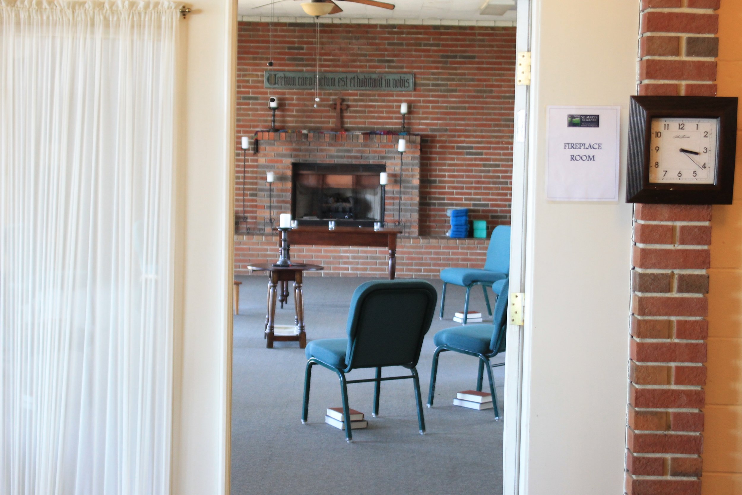 A room with a brick fireplace, stacked blue towels, blue chairs, a small table with candles, and a sign that reads 'FIREPLACE ROOM'.