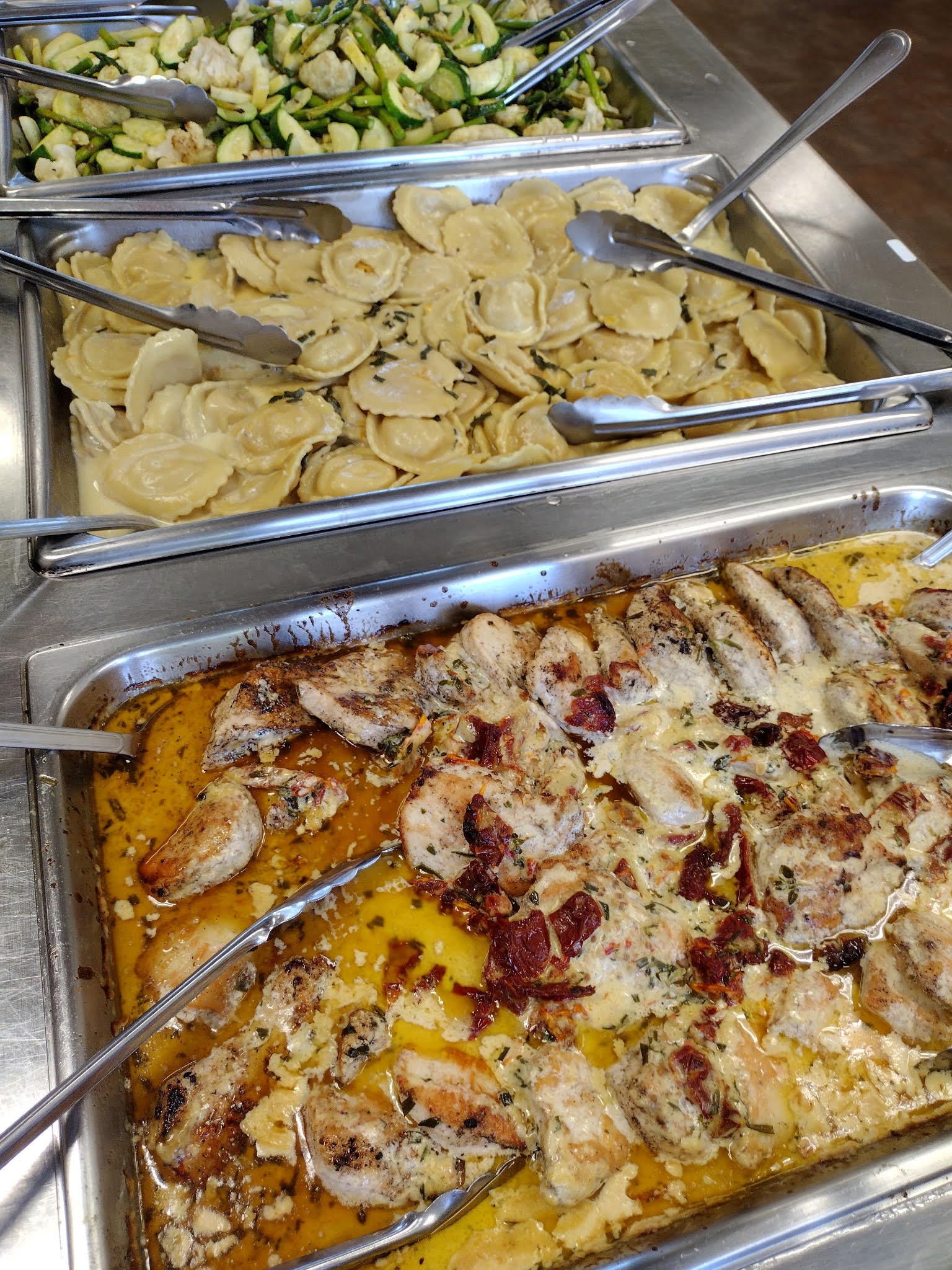 Buffet trays containing zucchini and cauliflower salad, cheese ravioli, and chicken with herbs and sun-dried tomatoes.