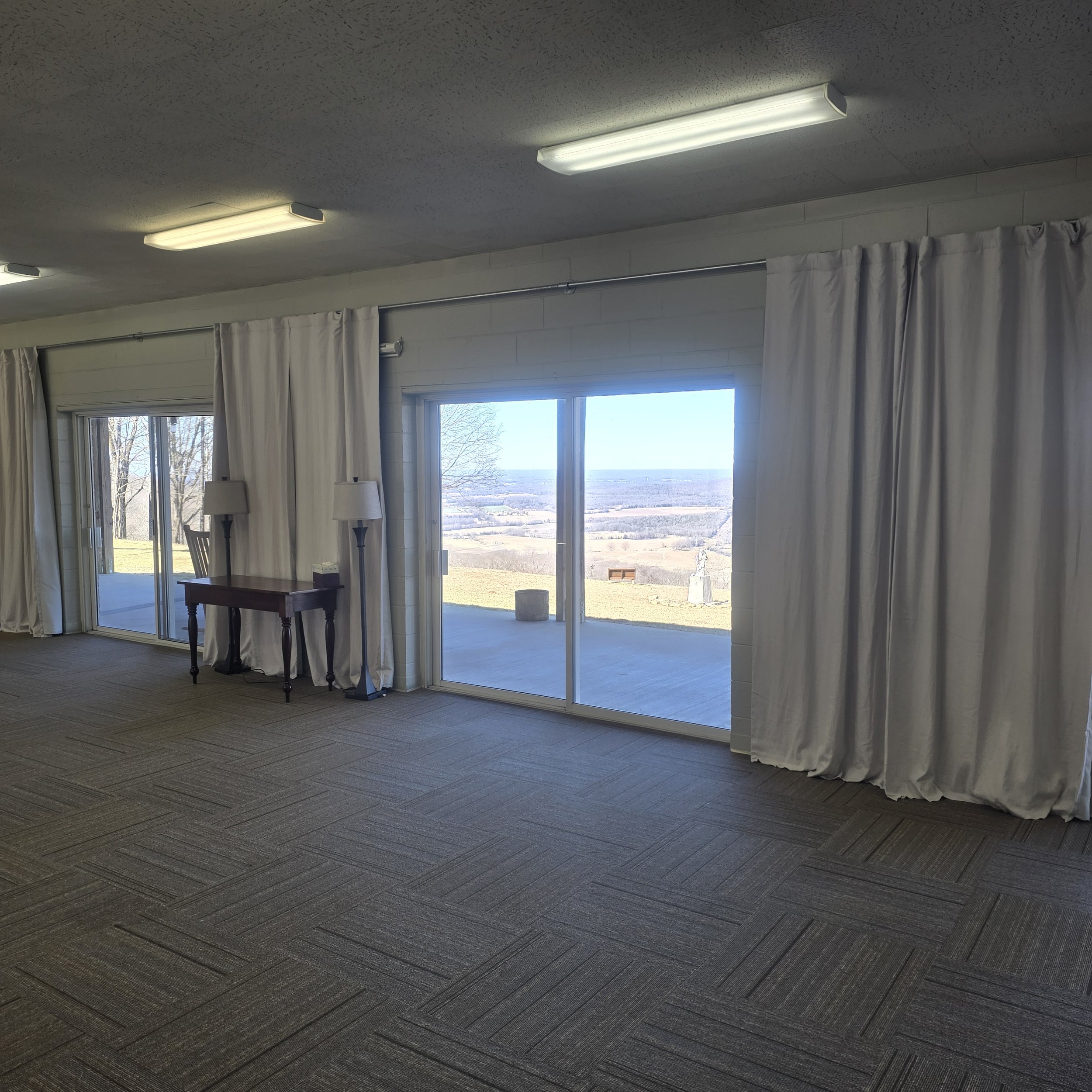 Room with sliding glass doors and white curtains, view of a hilly landscape and clear sky outside.