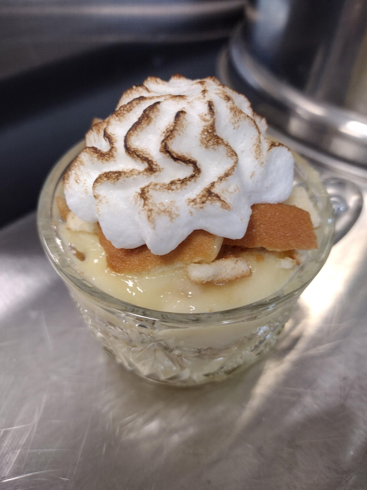 A dessert in a glass dish topped with whipped cream and sprinkled with cocoa powder, with slices of apple and cinnamon underneath.