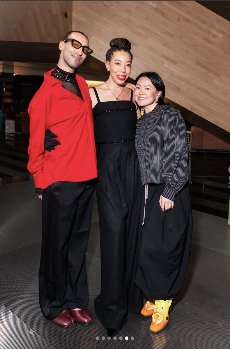 Three people posing indoors, wearing stylish black and red outfits, smiling at the camera.