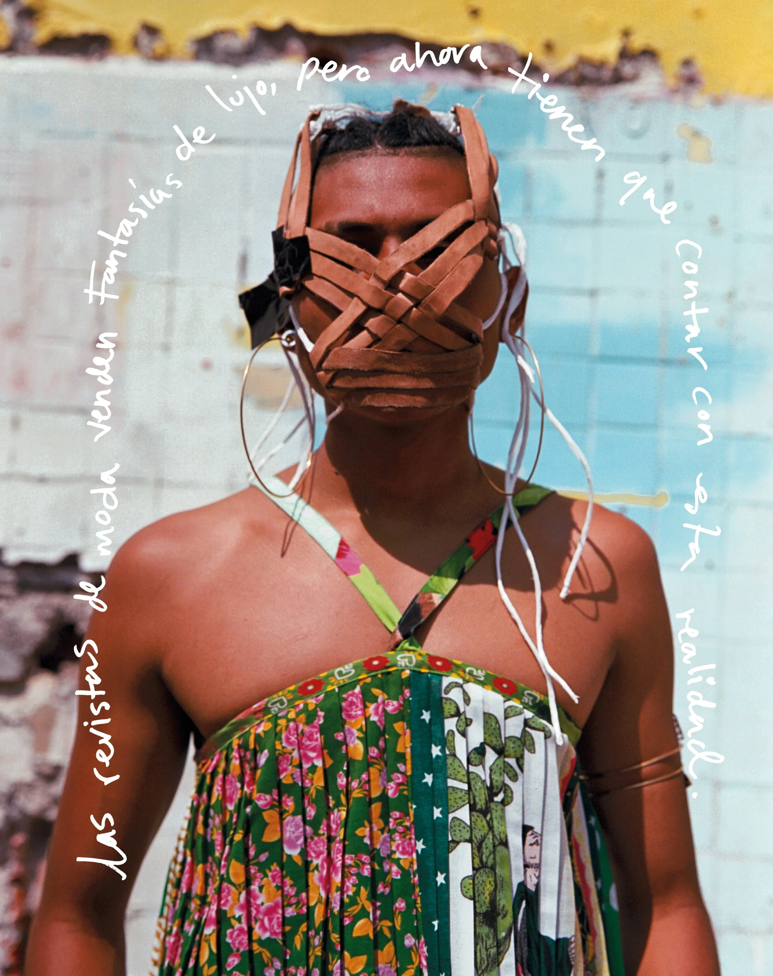A woman wearing a colorful, floral dress and large hoop earrings stands outdoors with a distressed wall in the background. She has a woven mask over her face and a caption in Spanish curved around her head, translating to "I always wanted to see the 