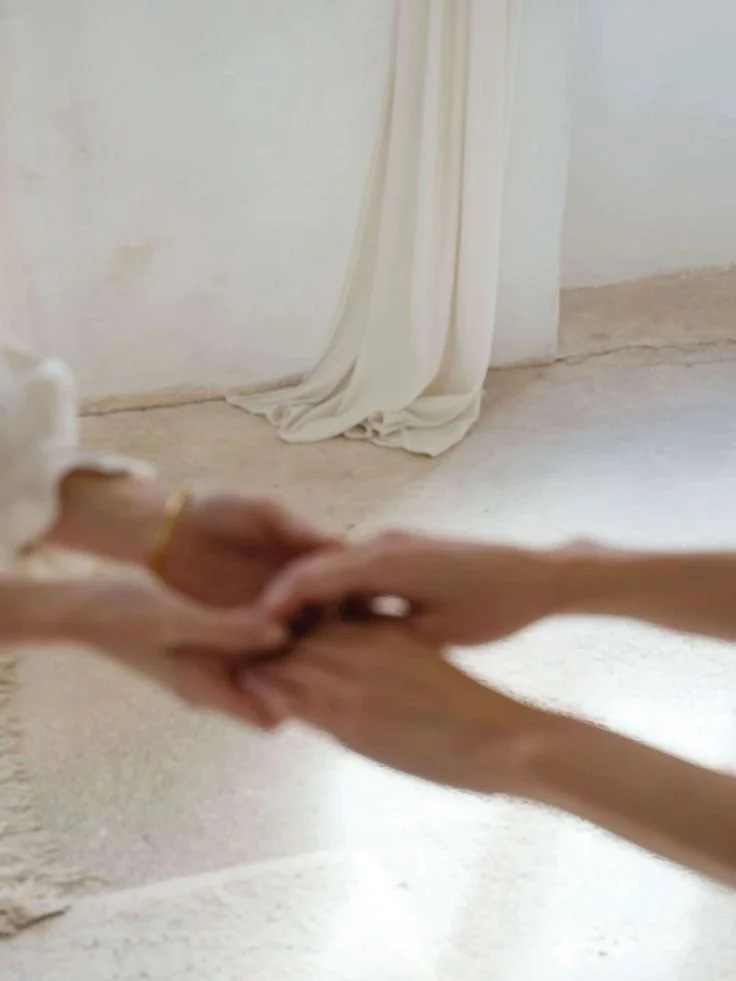 Two hands holding in a room with white curtains and a beige floor.