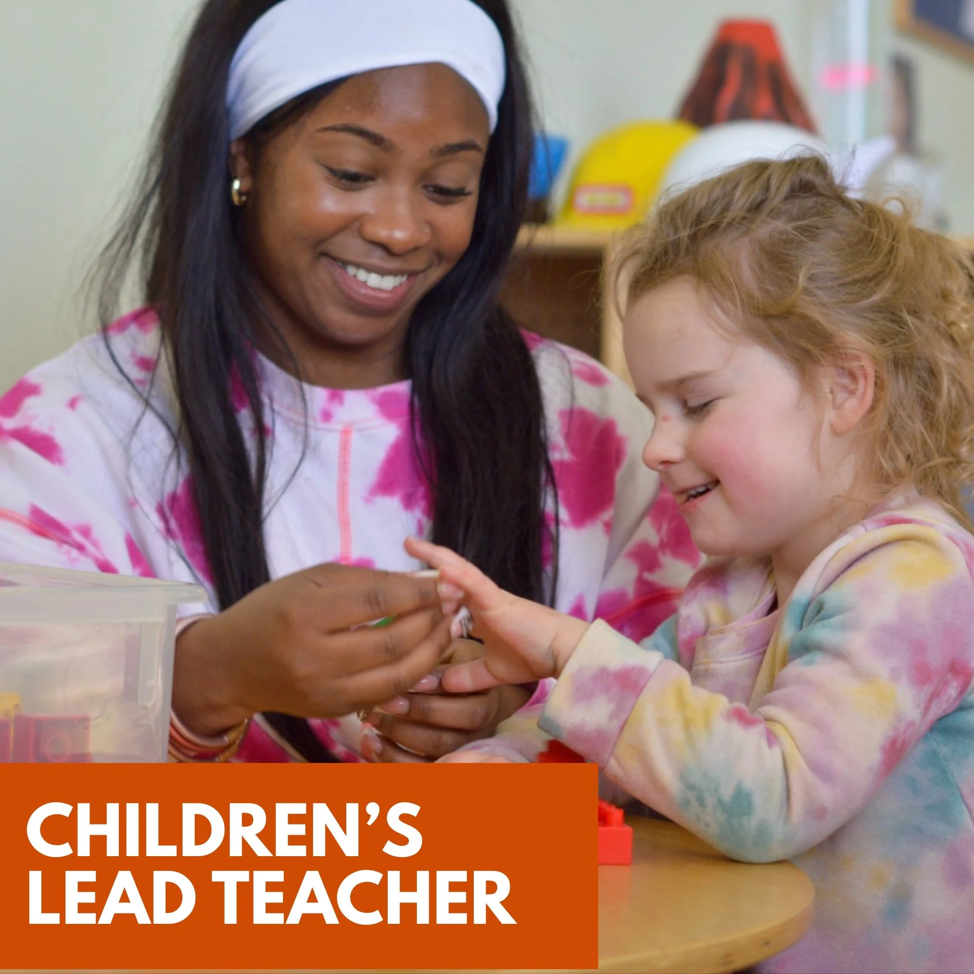 A young woman and a young girl are smiling and engaging in a hands-on activity at a table in a classroom setting. The woman appears to be a teacher, and the girl is a student. The text overlay reads 'Children's Lead Teacher.'