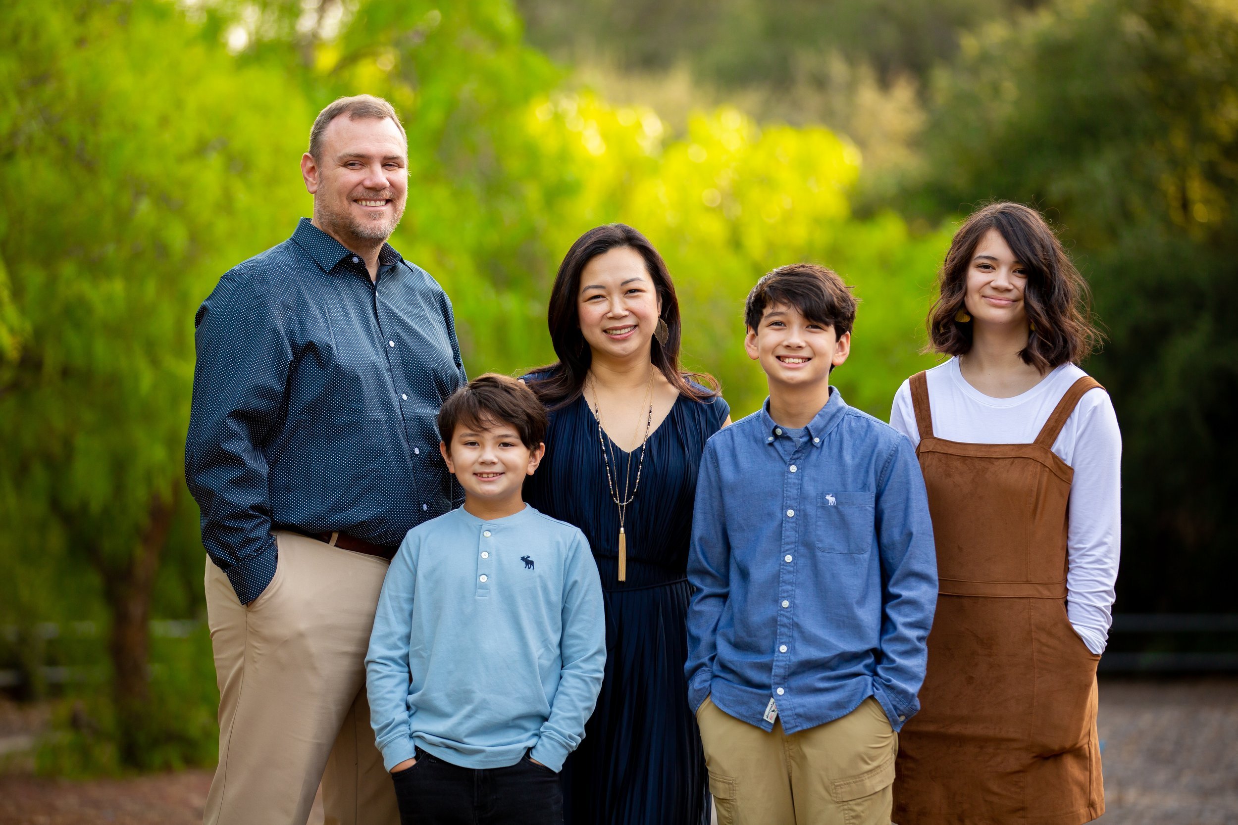 Family poses for picture with greenery in the background.