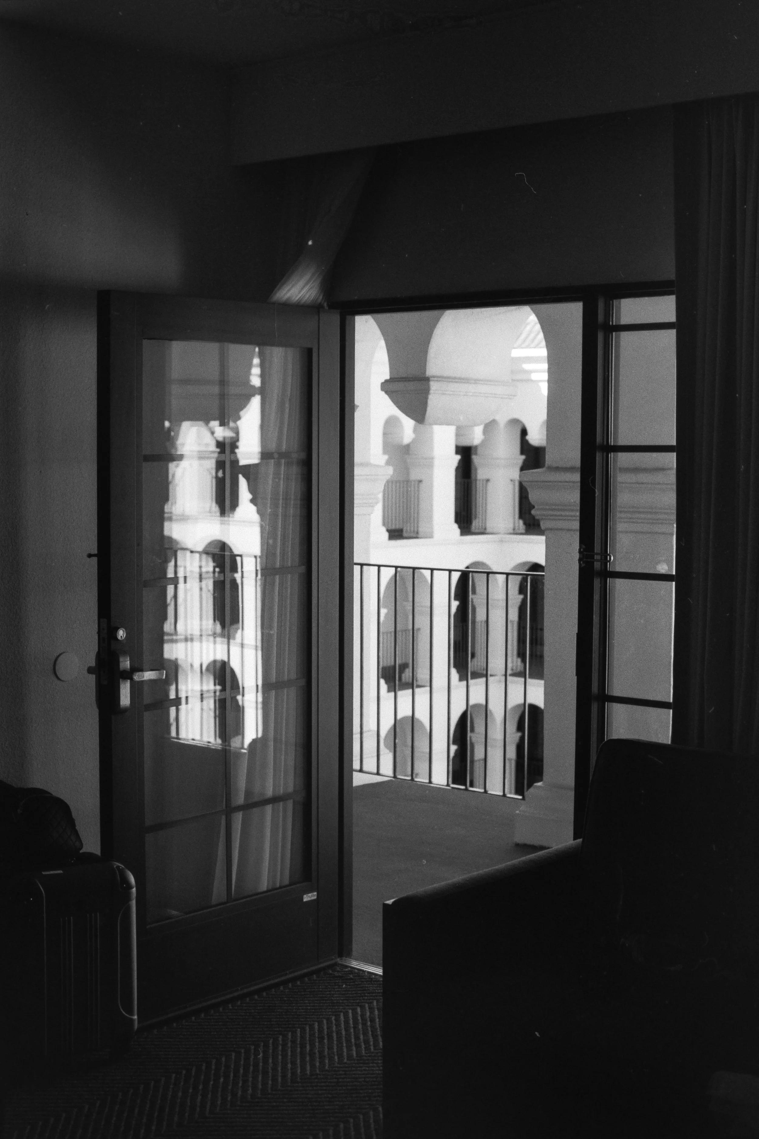 Black and white photo of an open glass door leading to a balcony with arches and columns in the background.