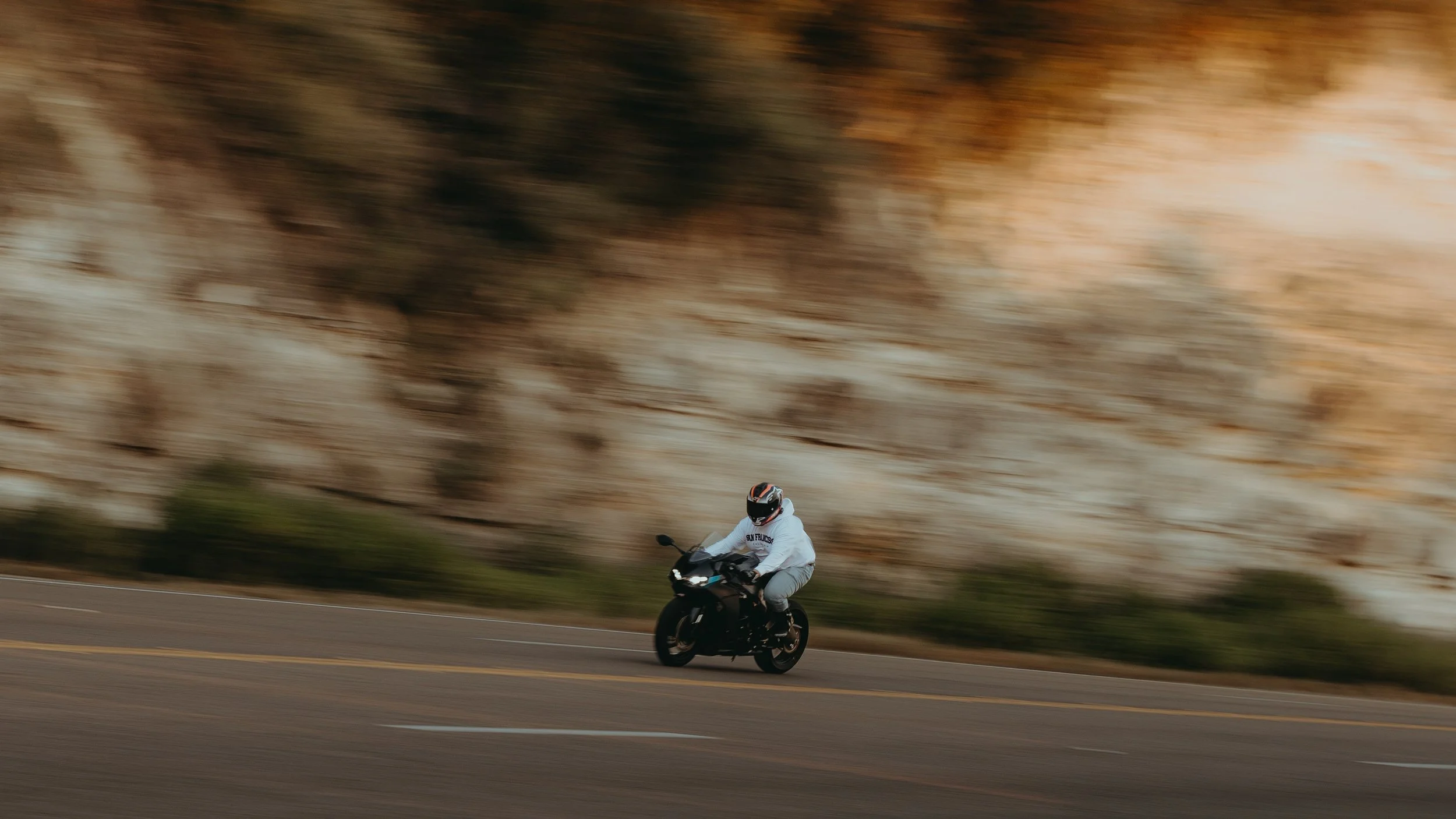 A person riding a black motorcycle on a road with a blurred rocky cliff background.