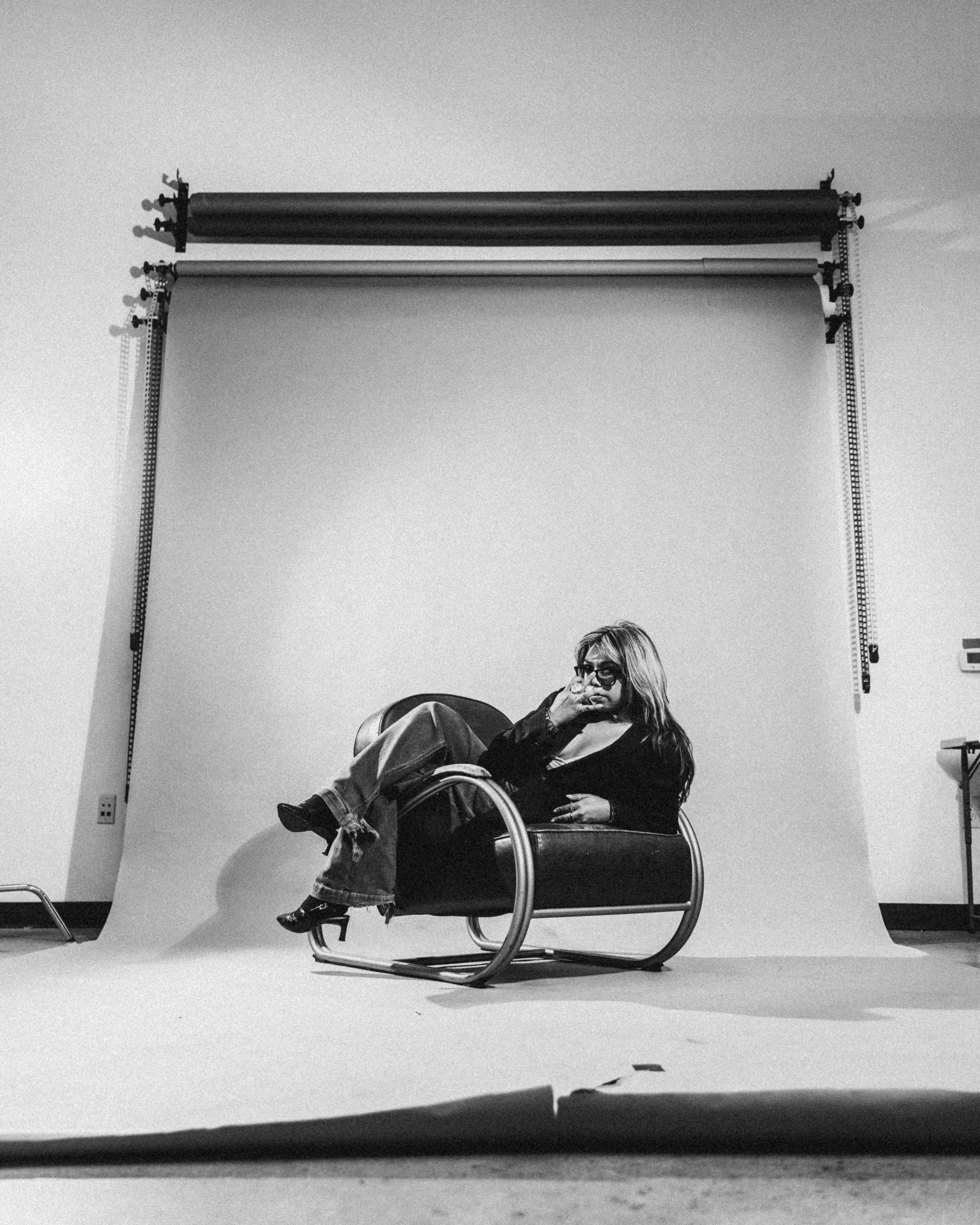 Black and white photo of a woman sitting in a modern chair in front of a photography backdrop in a studio.