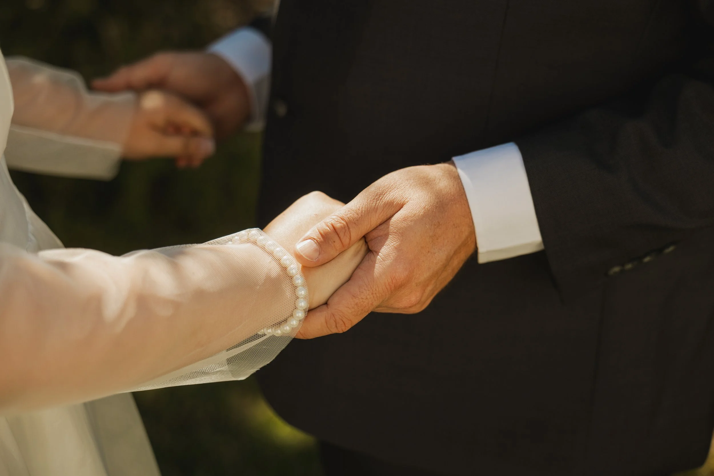 Close-up of a bride and groom holding hands during their wedding ceremony.