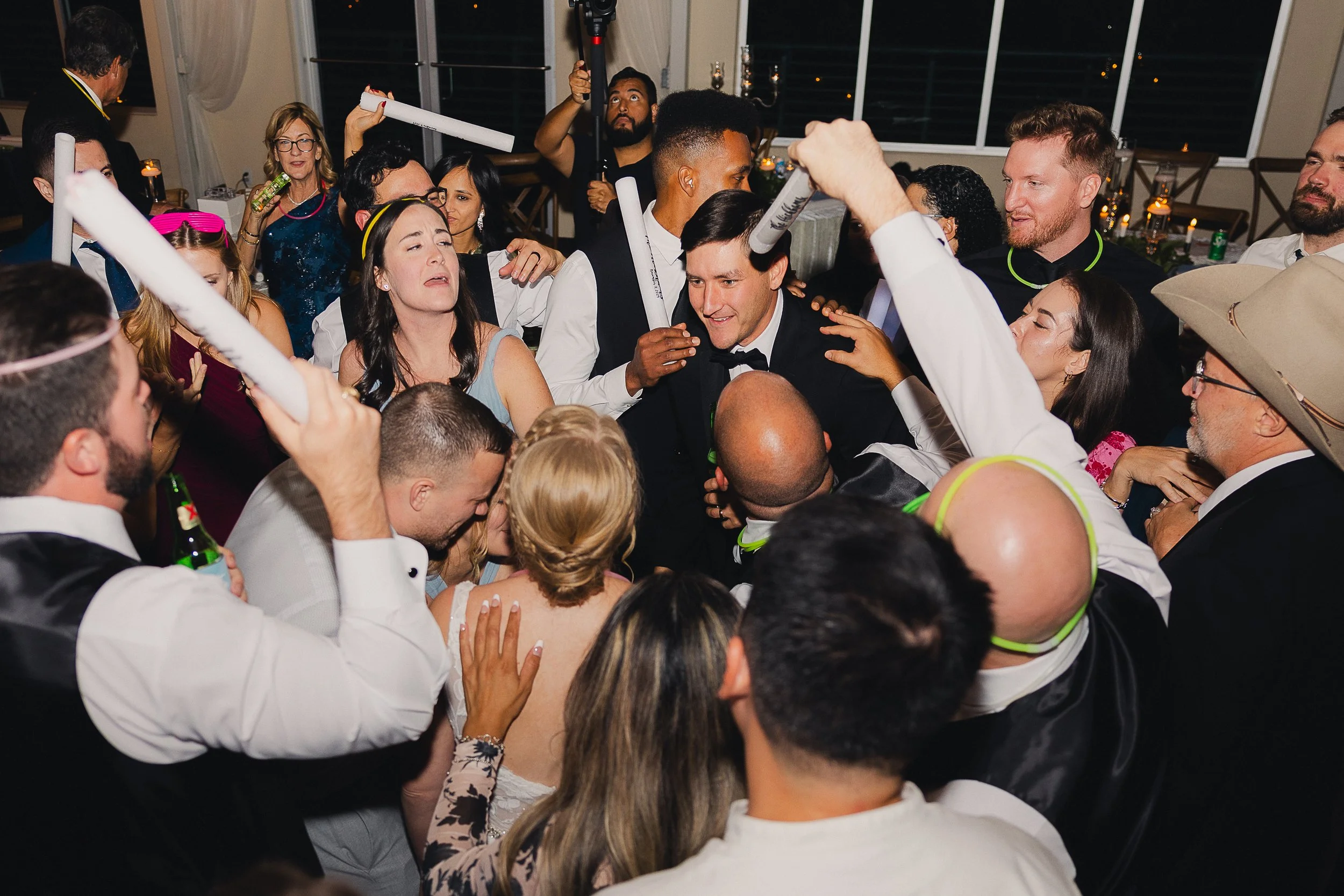 People dancing and celebrating at a lively party, with some holding glow sticks and wearing party accessories.