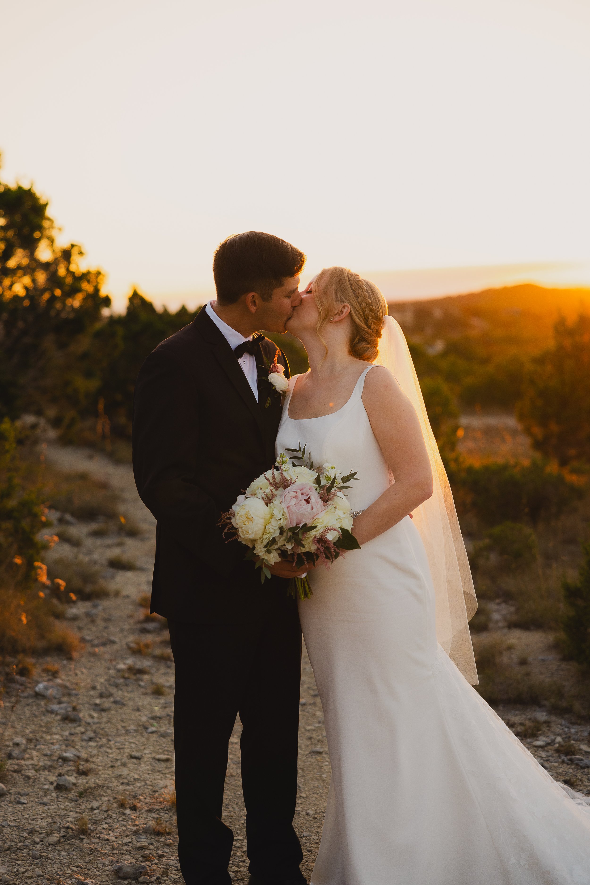 A bride and groom share a kiss during their wedding at sunset outdoors.