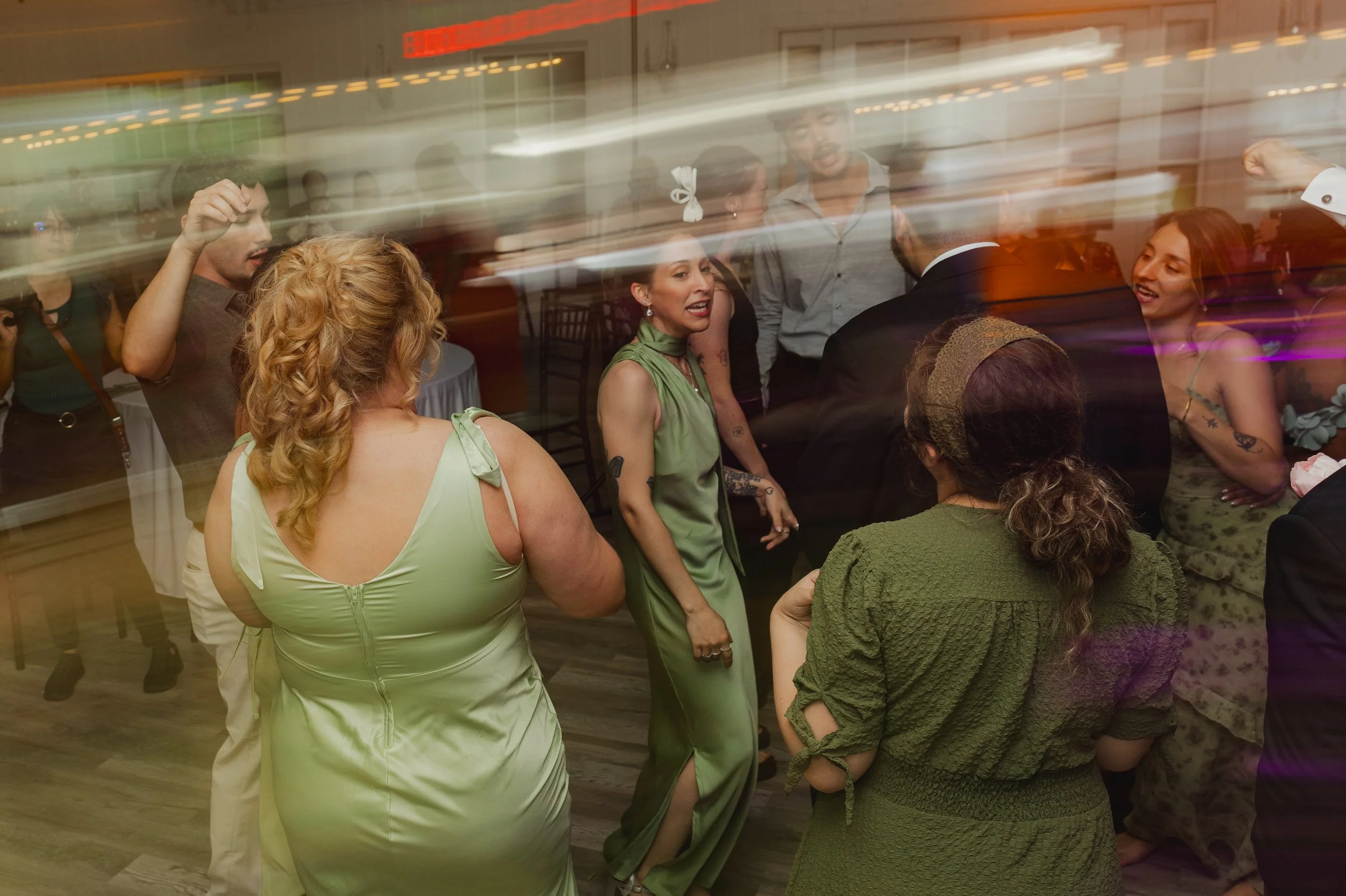 People dancing and socializing at a party or celebration, some with tattoos, dressed in stylish attire, with colorful lighting and motion blur