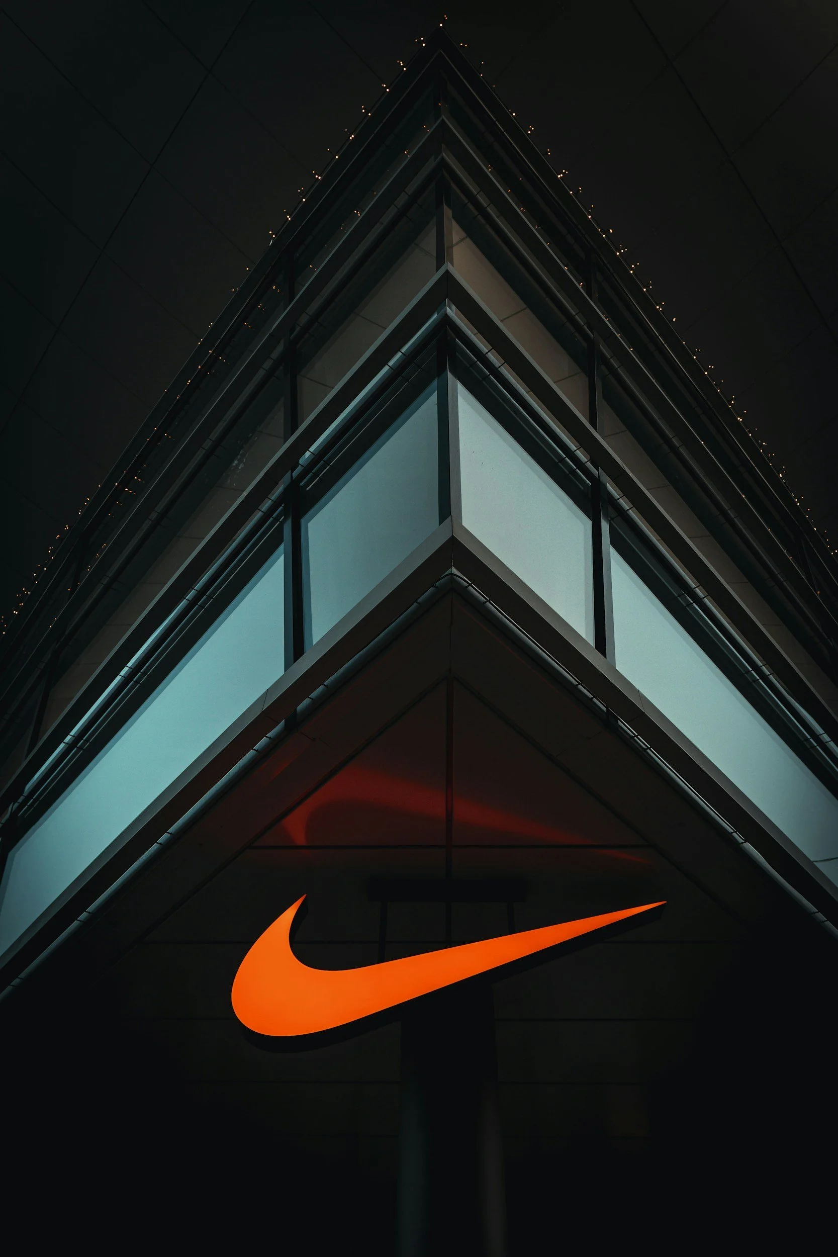 Modern building with illuminated windows and a prominent orange Nike logo sign below.
