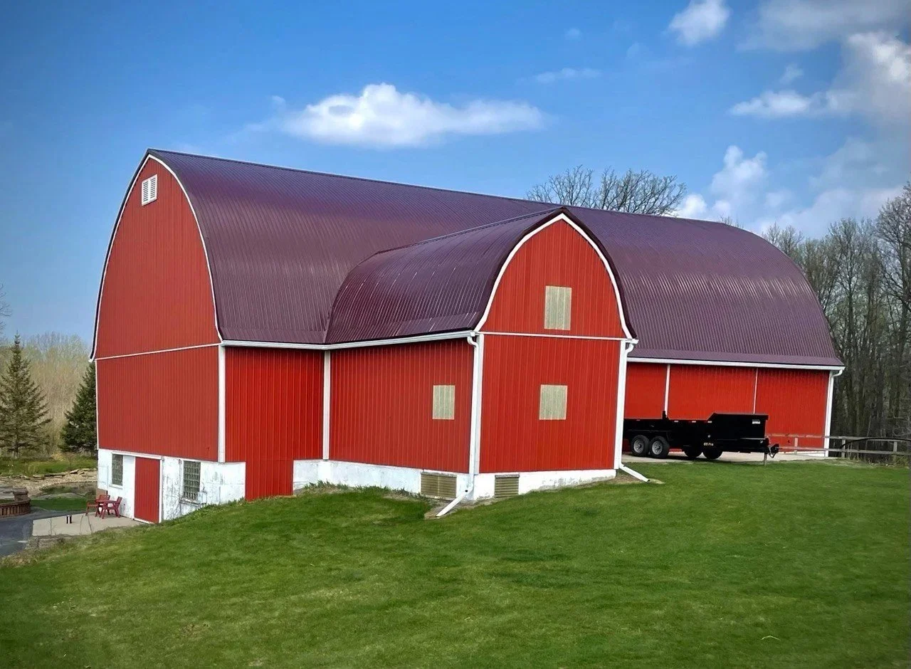 red barn with maroon standing seam metal roof on a grassy hill with blue skies in spring