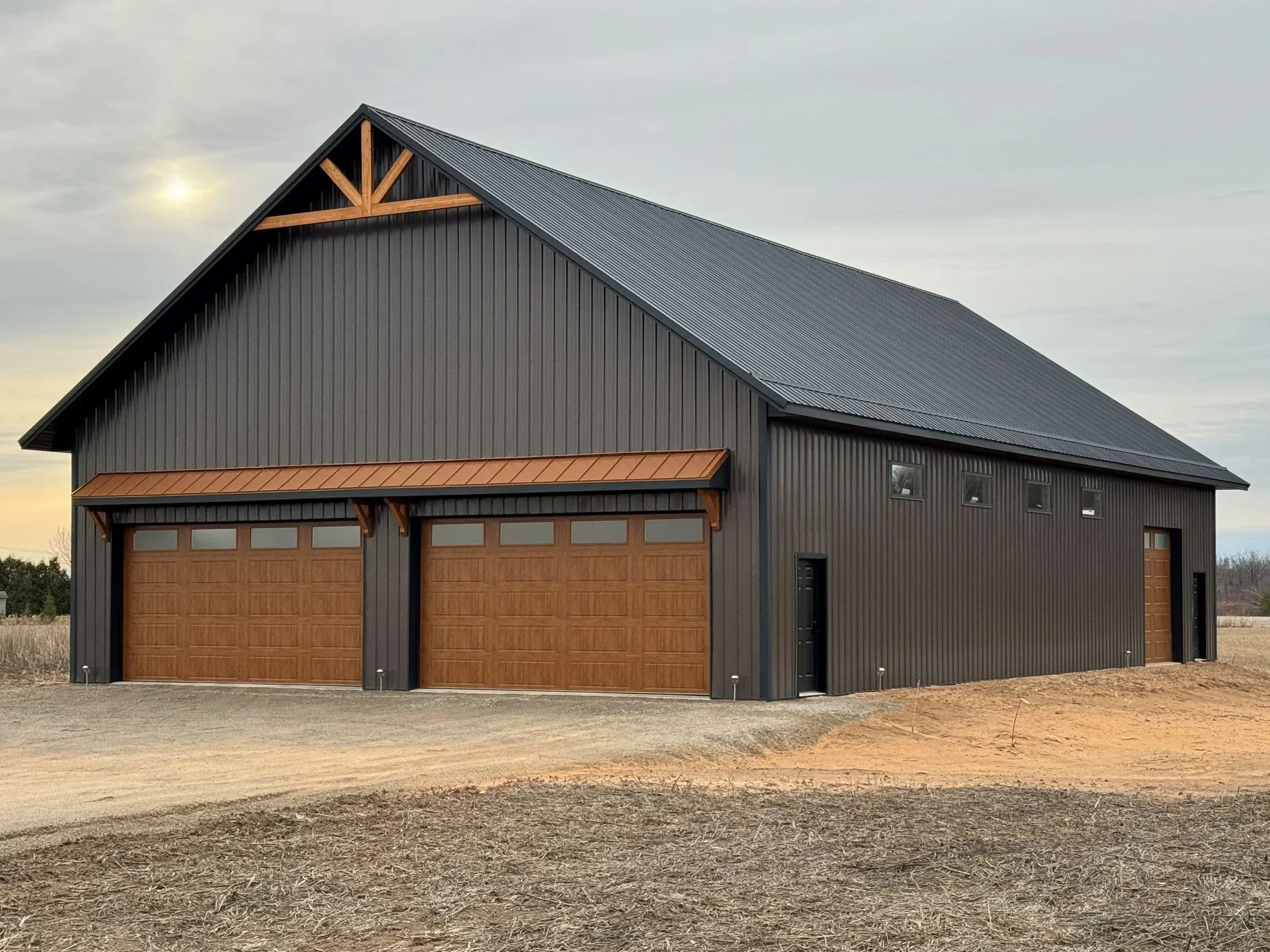 standing seam burnished slate metal roofing and siding with wooden gable accent, wooden overhead garage doors, and black service doors and copper metal roofing accents