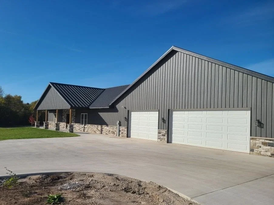 black board and batten steel siding home with black standing seam steel roof and white overhead garage doors