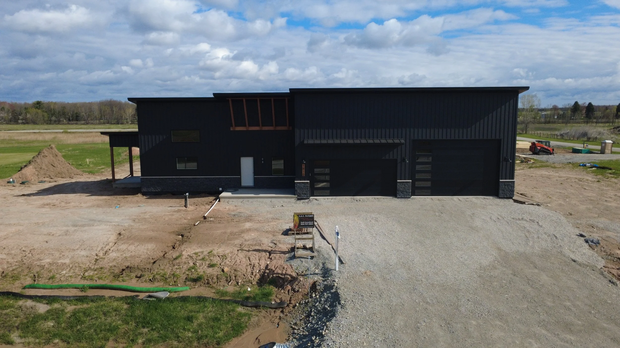 Black metal roofing and metal siding on barndo minium with wood and stone accents in a green and brown field in spring in Wisconsin