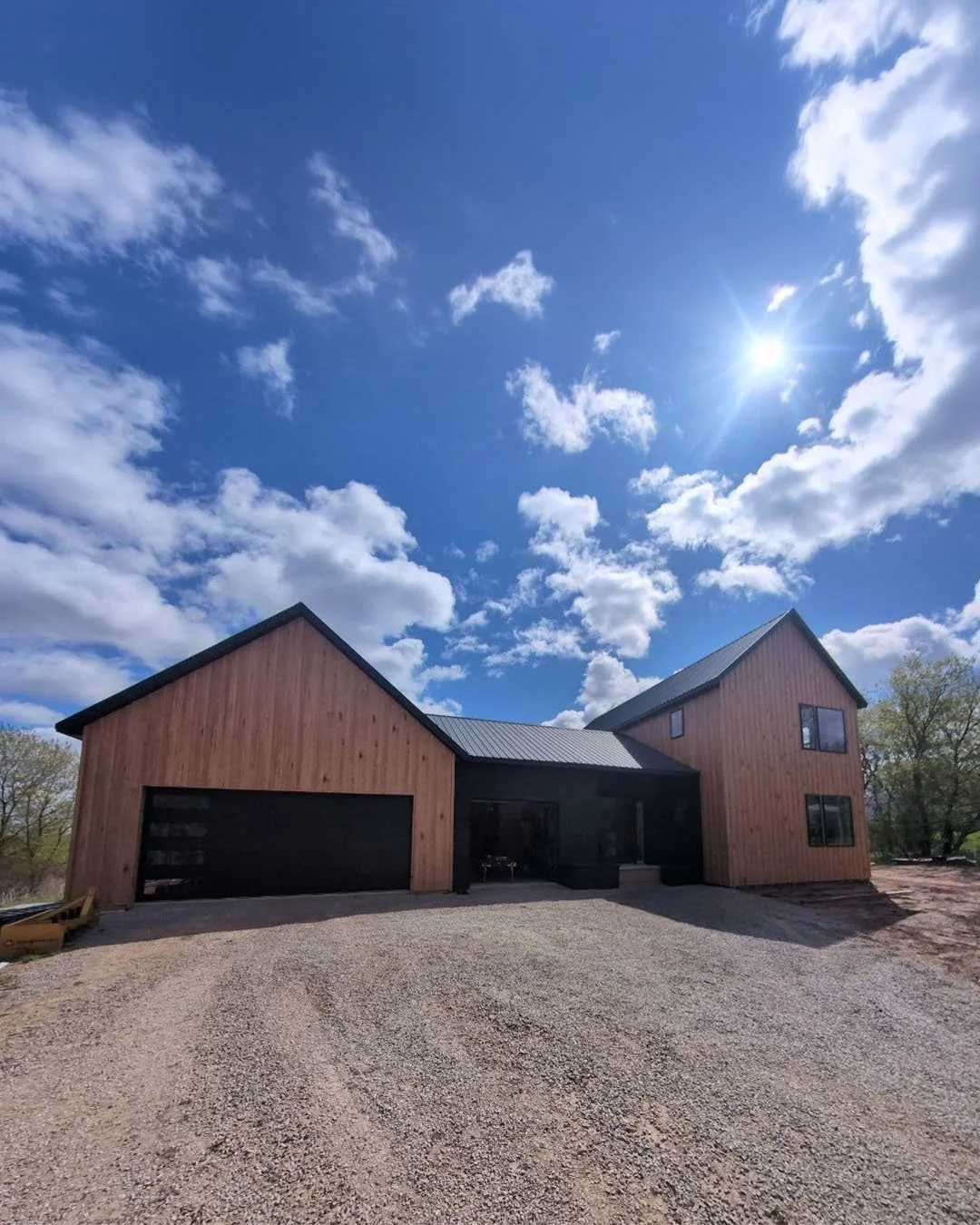 Wood textured board and batten steel siding with black standing seam roof and modern overhead garage doors and architecture