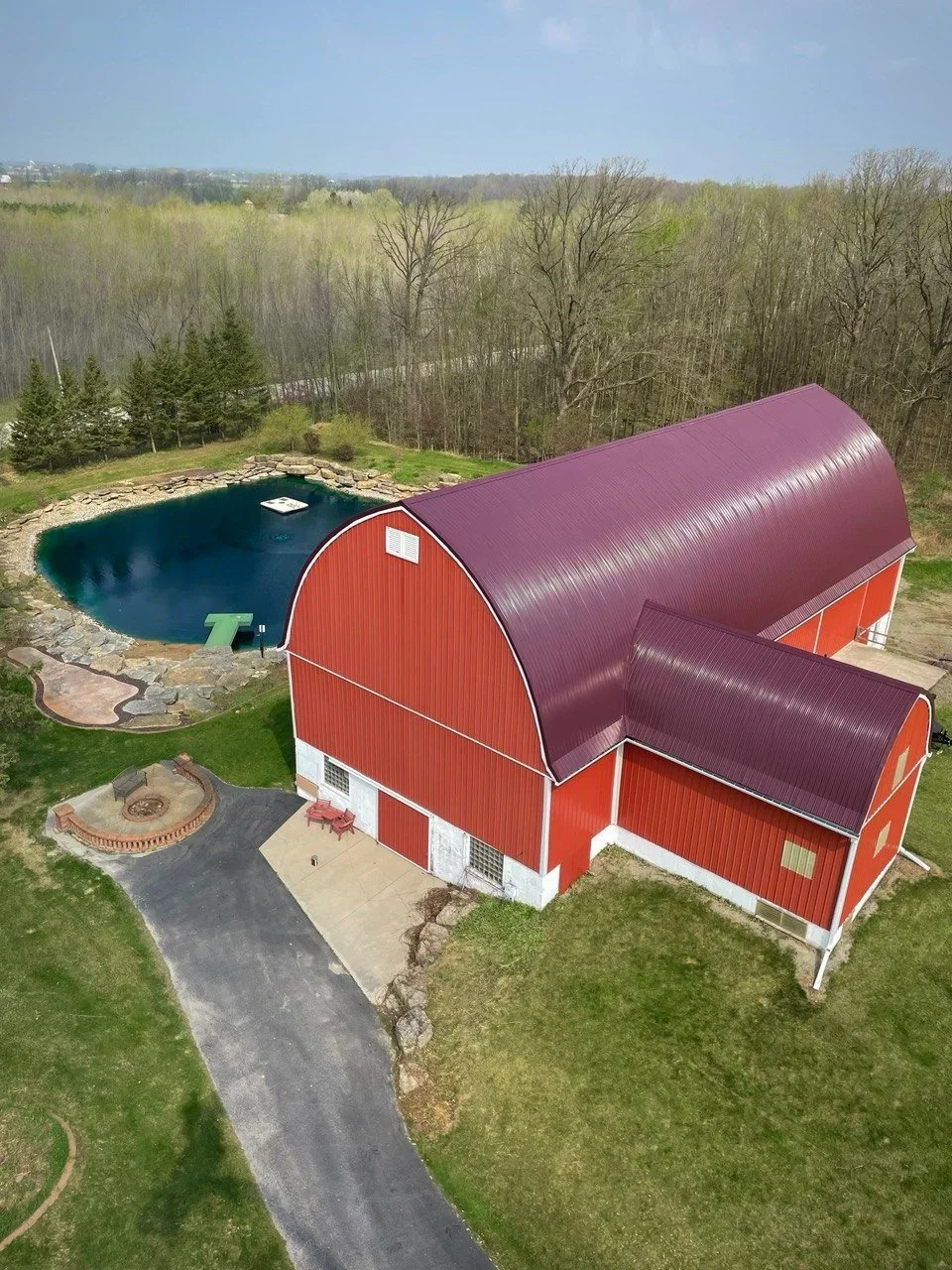 large red barn with maroon standing seam curved roof on a grassy hill with a blue swimming pond