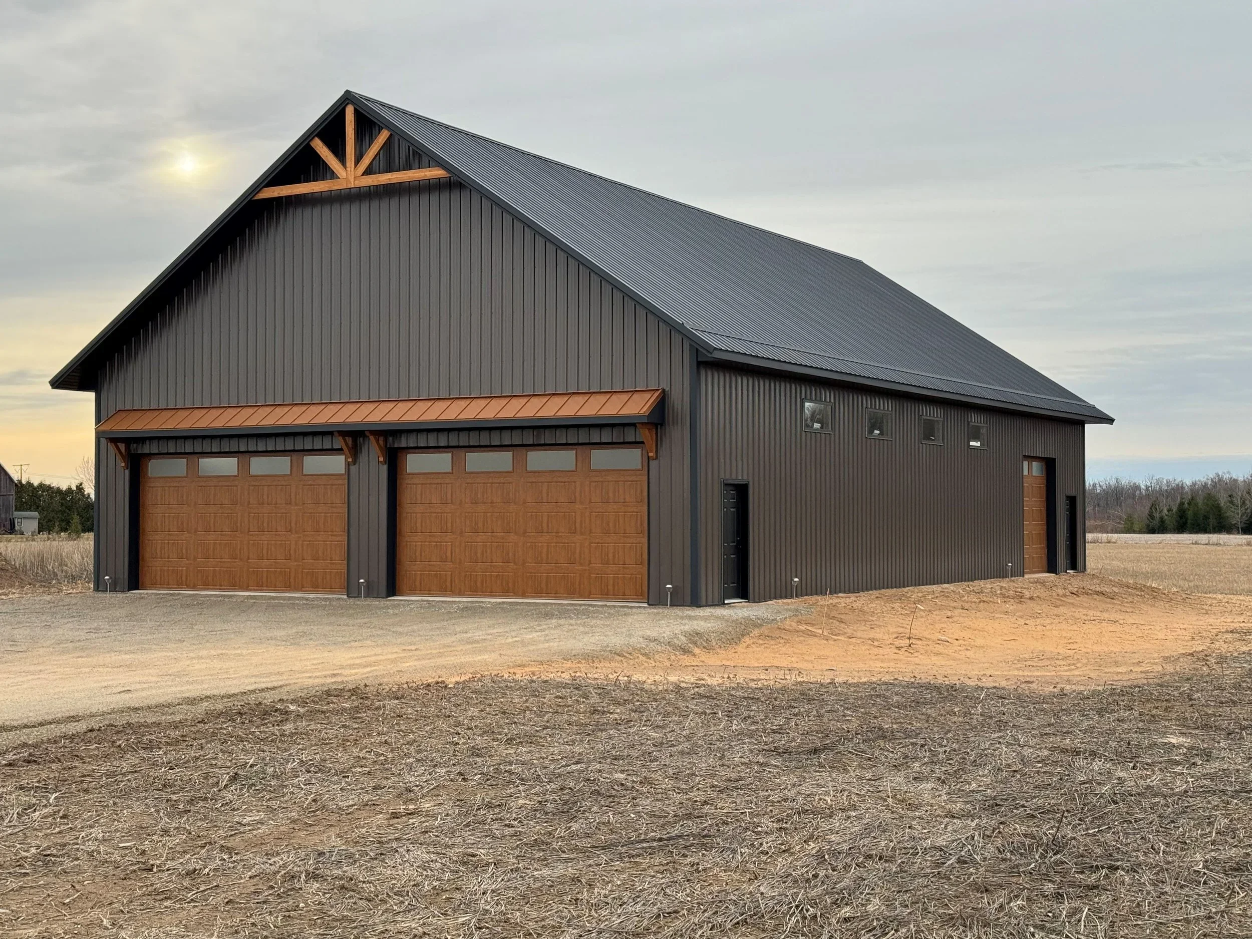 standing seam burnished slate metal roofing and siding with wooden gable accent, wooden overhead garage doors, and black service doors and copper metal roofing accents