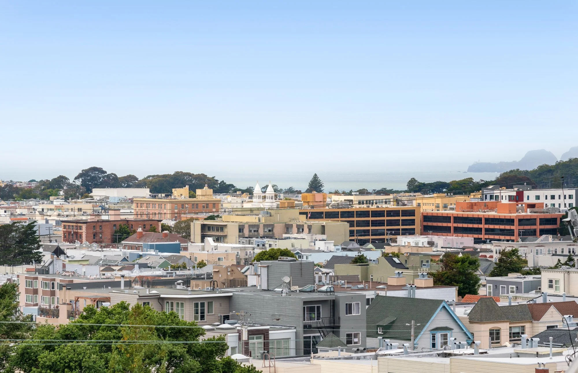 Cityscape of residential and commercial buildings with the ocean and fog in the background under a clear sky.
